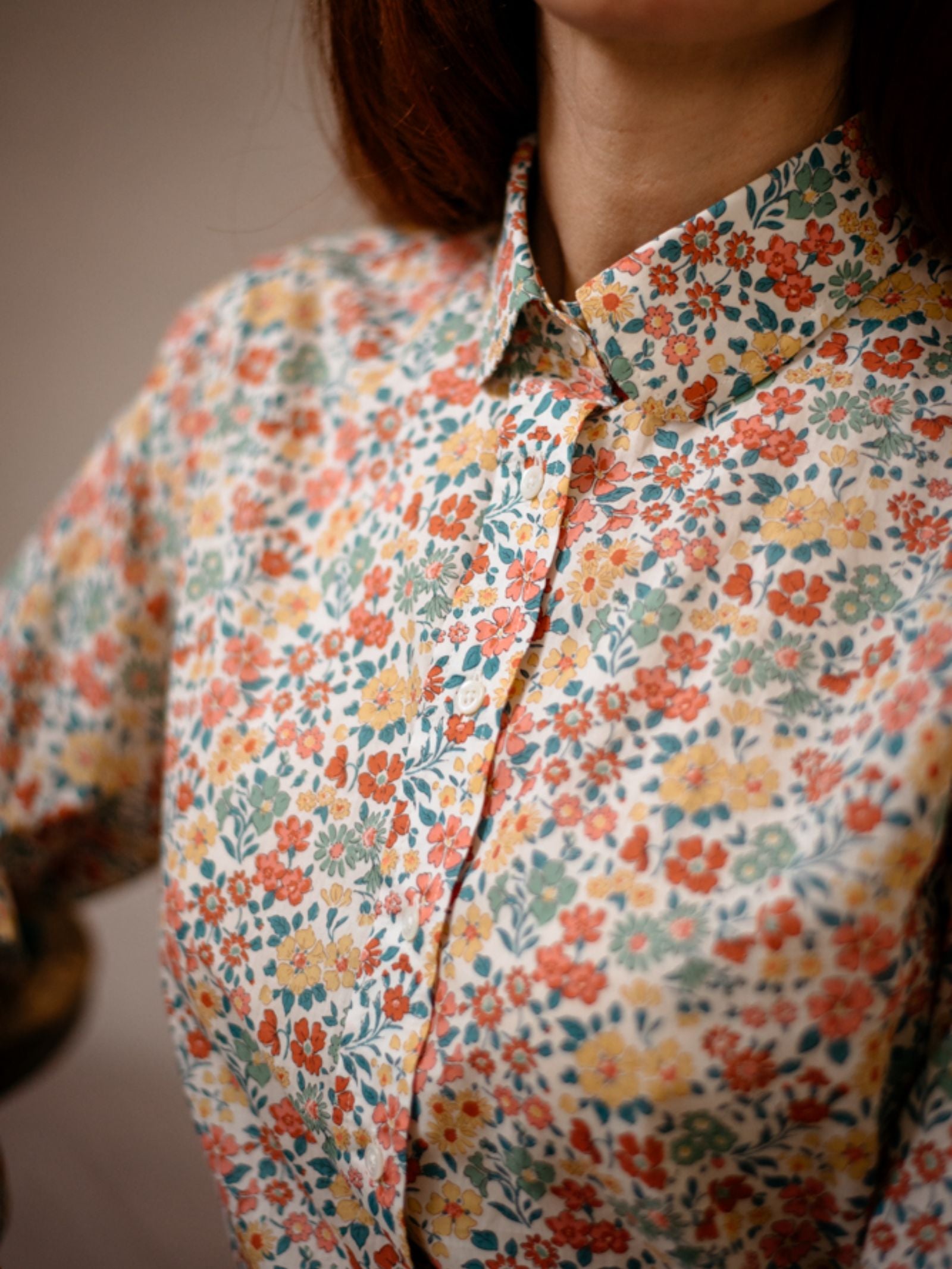 A person wears a vibrant Campbells of Beauly Liberty Print Cotton Shirt, crafted from Tana Lawn cotton and featuring a colorful floral pattern in red, yellow, blue, and green; the photo highlights the upper torso and collar.