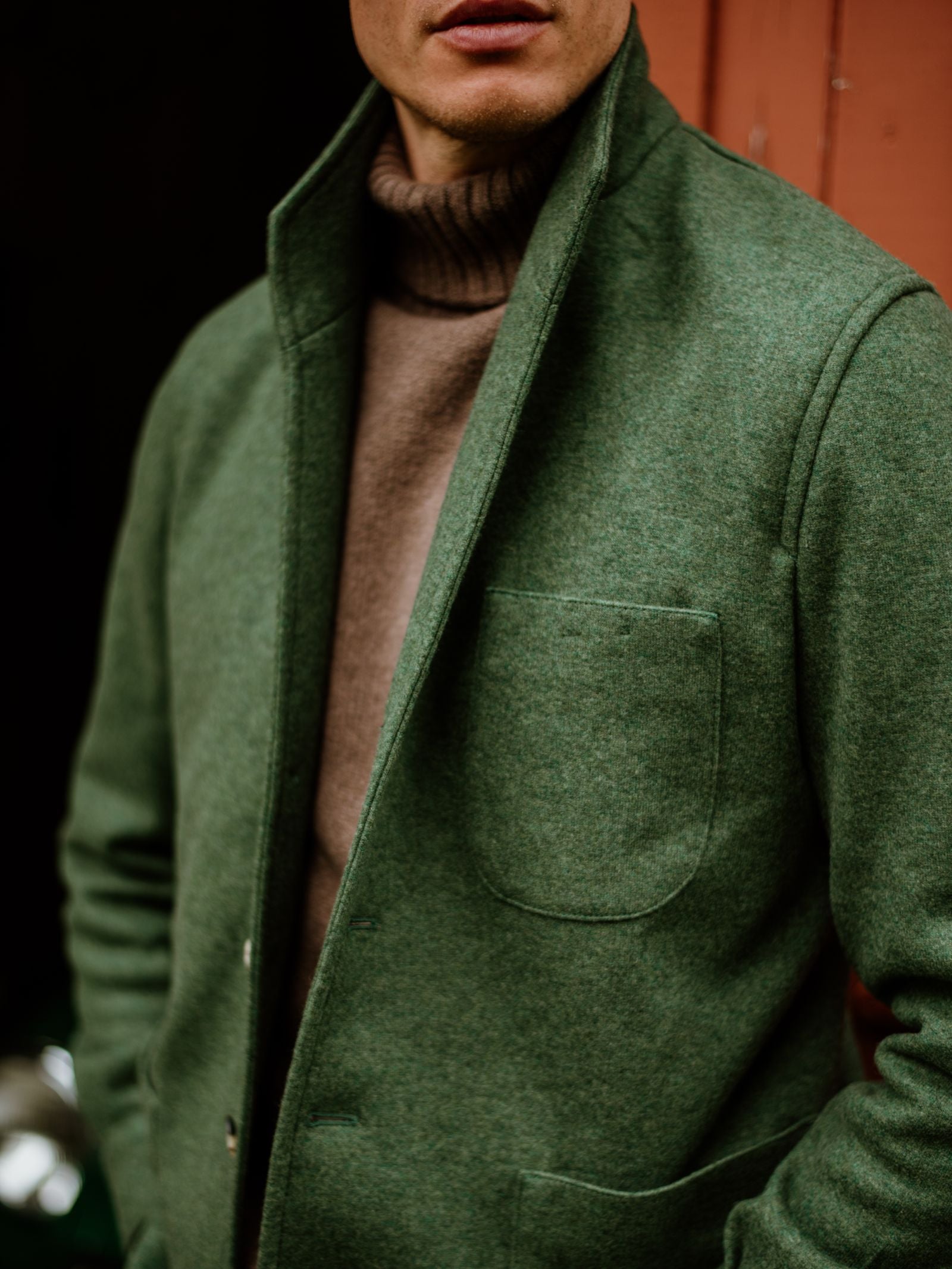 A person in a green Campbell's of Beauly Cashmere Teba Jacket over a brown turtleneck stands before a reddish-brown background, with the image cropped to display only the lower face and upper body.