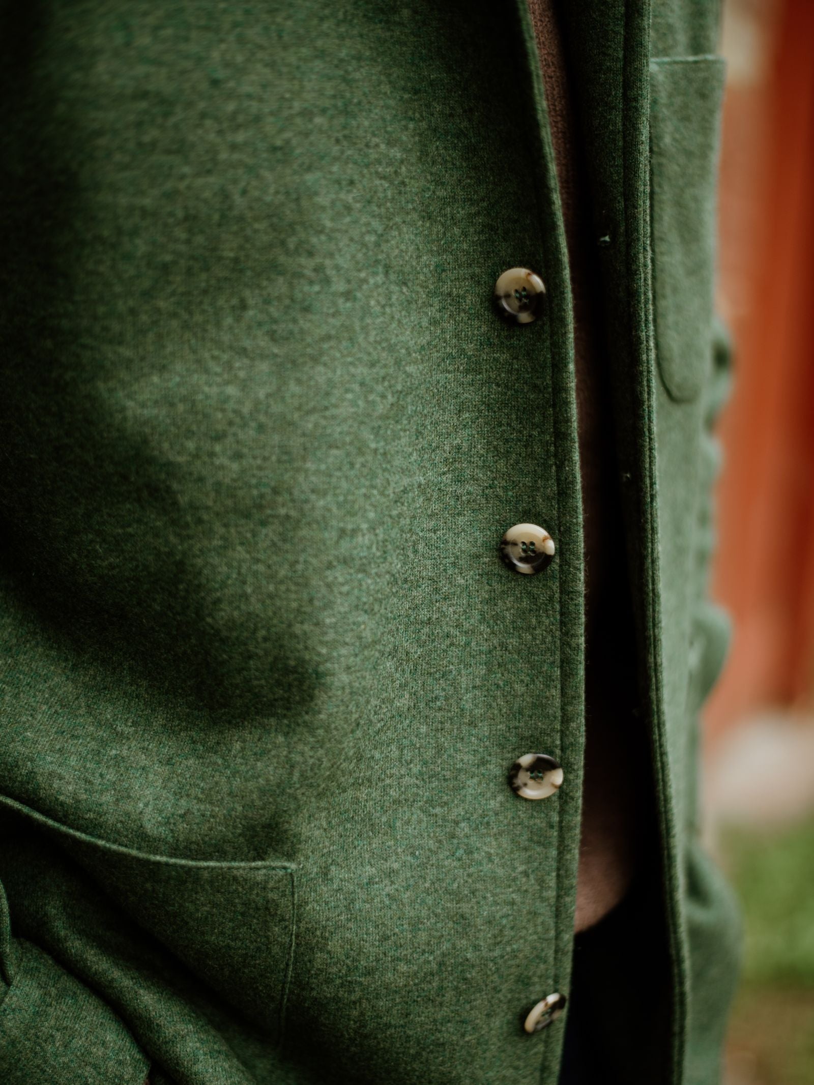 A close-up of Campbell's of Beauly Cashmere Teba Jacket in green, featuring large buttons and a pocket. The blurred background emphasizes the jacket’s distinctive texture and fine fabric details.