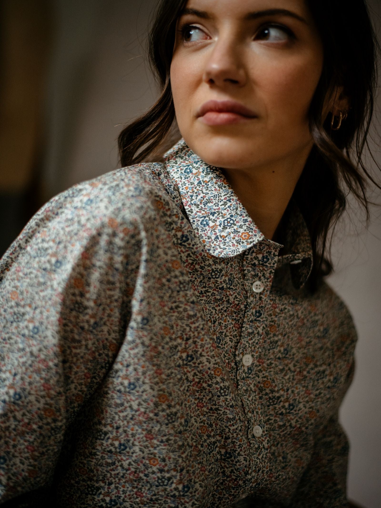 A woman with wavy brown hair looks off to the side, wearing the Campbells of Beauly Liberty Print Katie & Millie Shirt in a soft floral pattern against a neutral background.