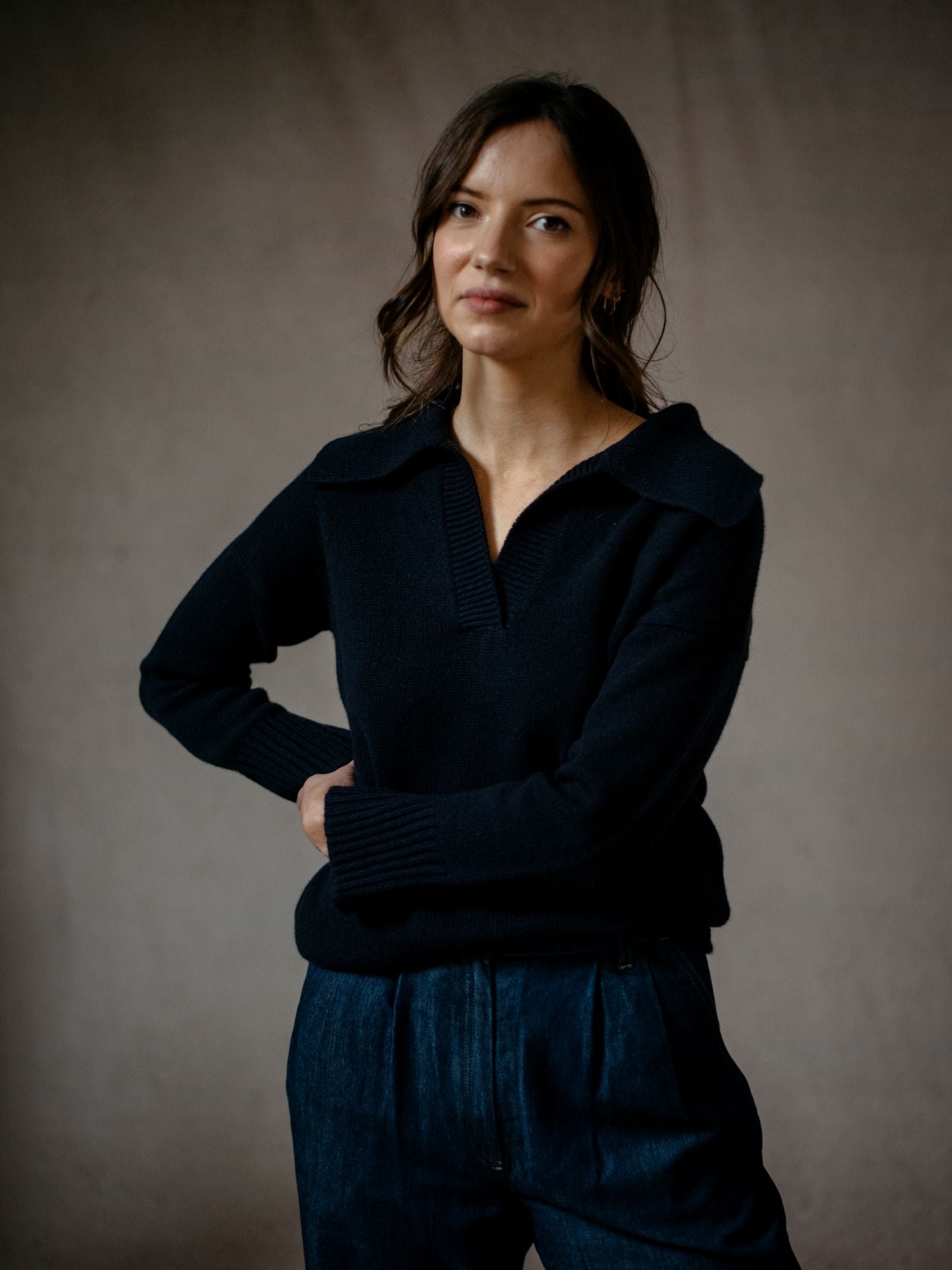 A woman with wavy brown hair models the Campbells of Beauly Cashmere Shirt Jumper, standing against a neutral background with her left hand on her hip and gazing softly at the camera.
