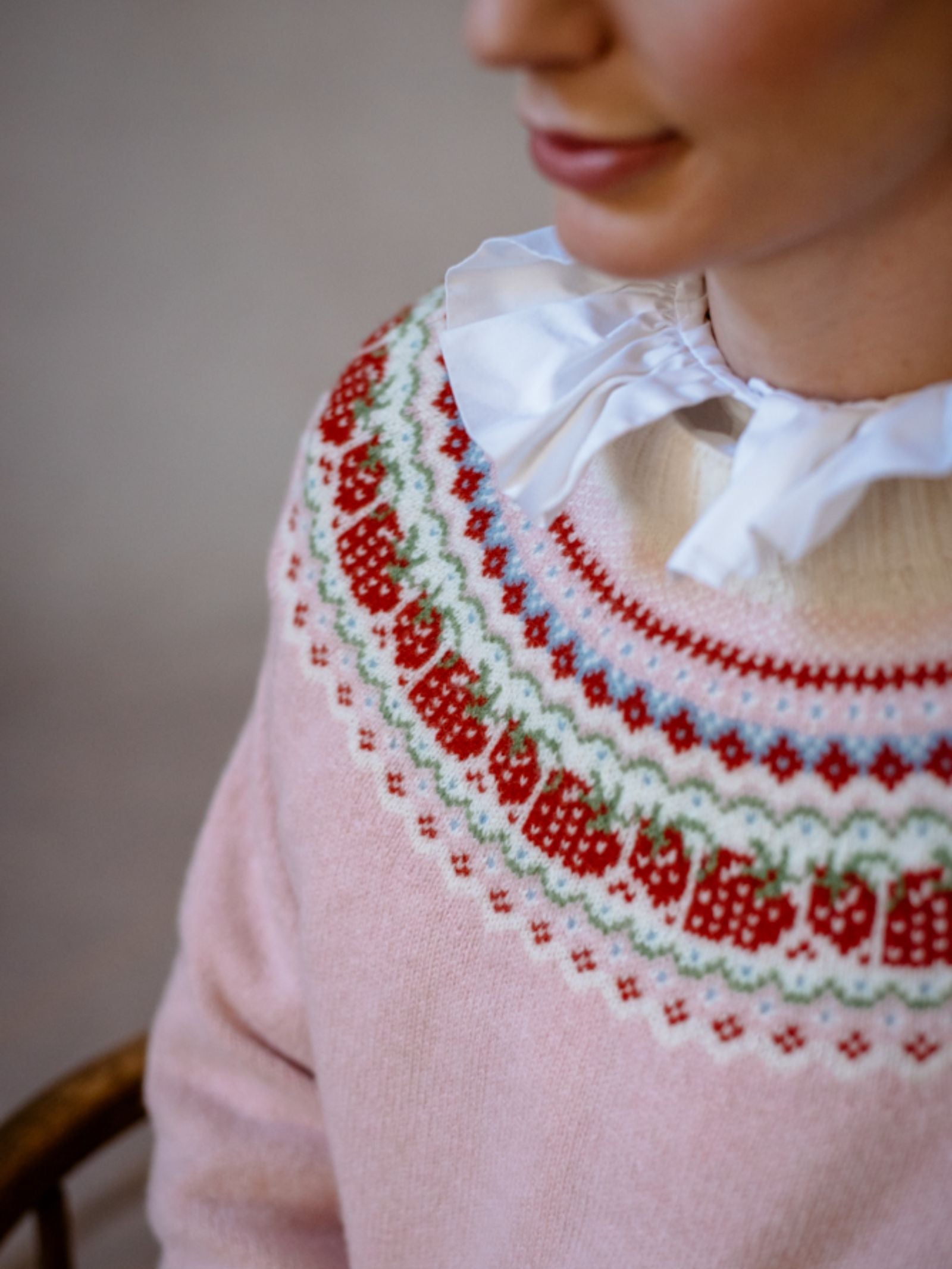 A person wears the Campbells of Beauly Geelong Lambswool Strawberry Yoke Jumper with a colorful Fairisle yoke, paired with a white blouse featuring a large ruffled collar.