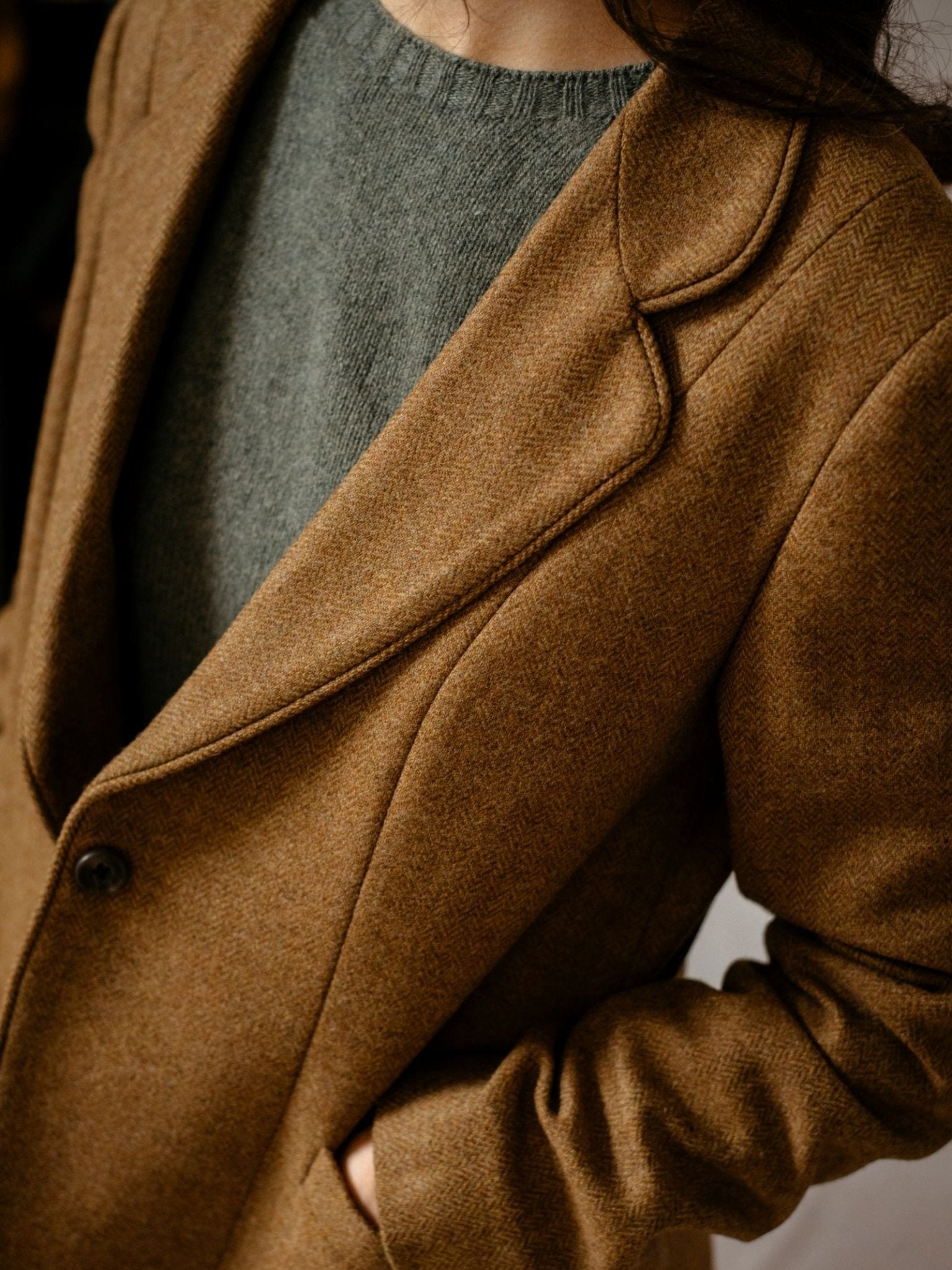 A person models the Campbells of Beauly House Jacket in brown herringbone tweed over a gray knit sweater, with one hand in a pocket. The image is cropped to display only the torso and part of the head.