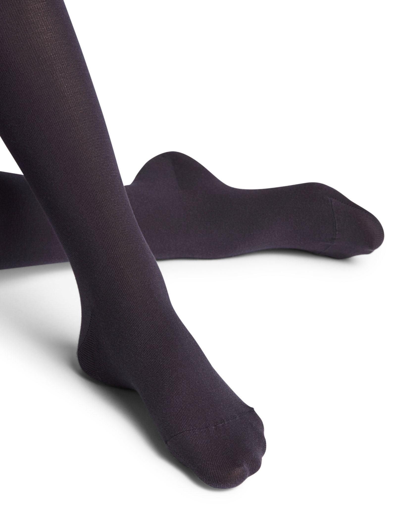 A person wearing FALKE Cotton Tights in navy sits with legs crossed on a white background, toes pointed and feet relaxed—crafted from sustainable cotton for comfort and style.
