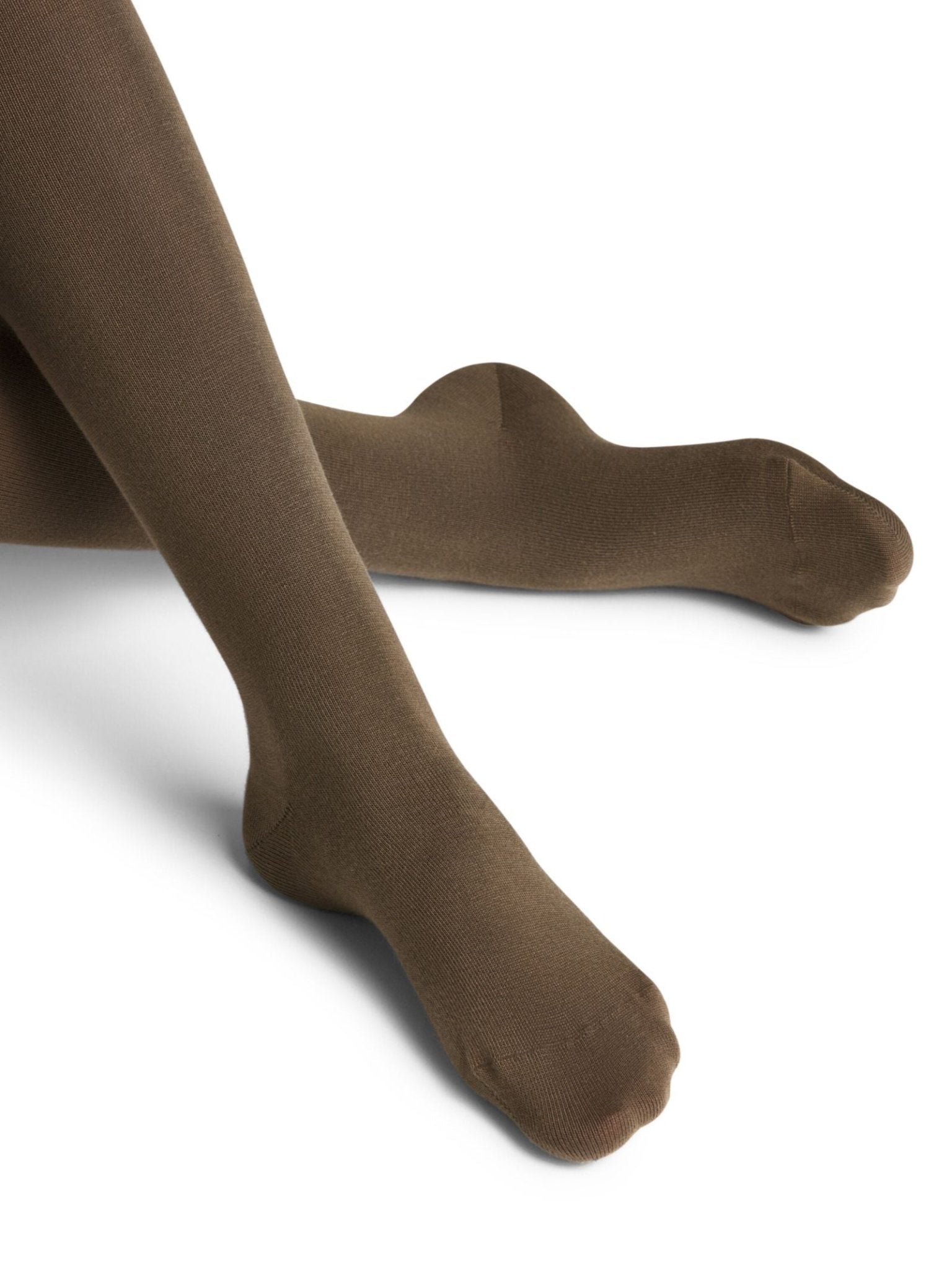 A person is seated with legs crossed on a white background, wearing FALKE Cotton Tights in Military Green. The sustainably made tights appear smooth and fitted.