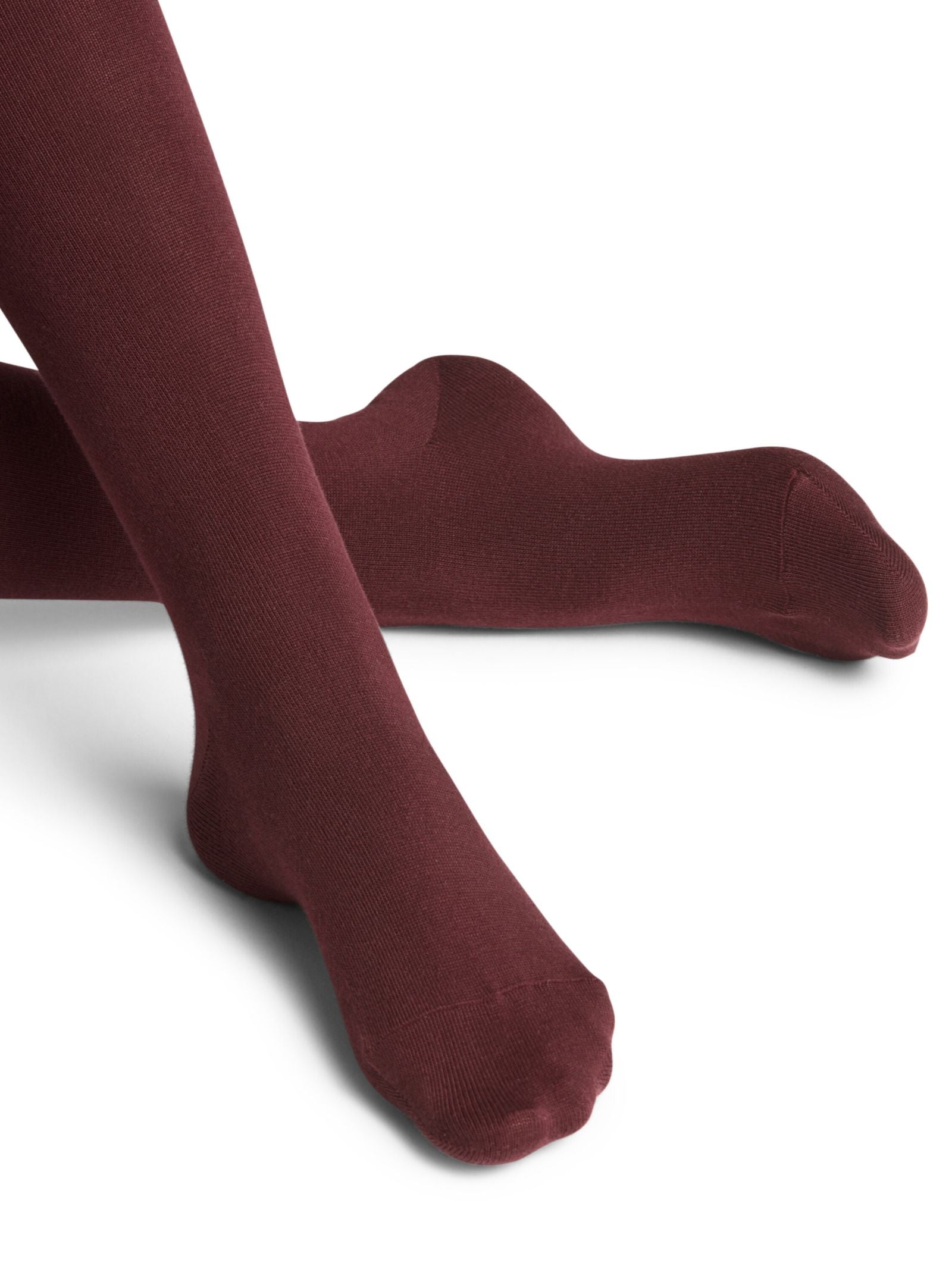 A person wears FALKE Cotton Tights in Barolo with legs crossed against a white background.