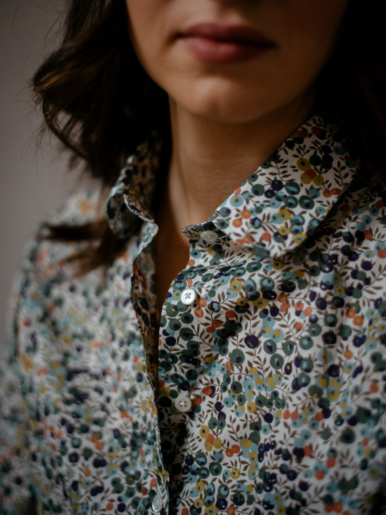 A close-up shows a woman in the Campbells of Beauly Liberty Print Cotton Shirt, highlighting its vibrant floral pattern on Tana Lawn cotton with her lips and part of her face visible.