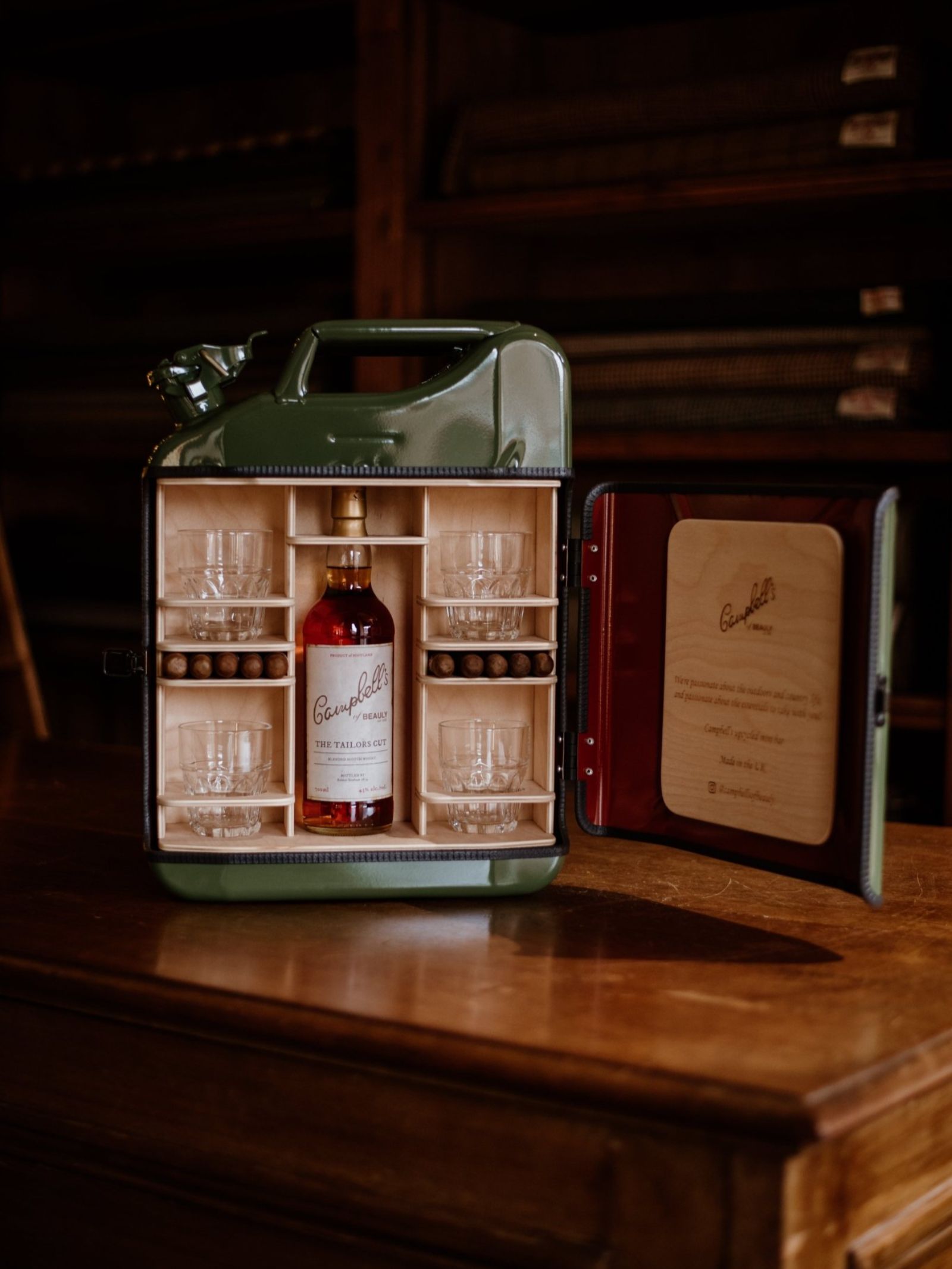 The Connoisseur Upcycled Mini Bar by Campbell's of Beauly is a UK-made green metal jerry can opening to whisky, four glasses, and snacks inside. The lid’s wooden panel features engraved text, making this a unique mini bar.