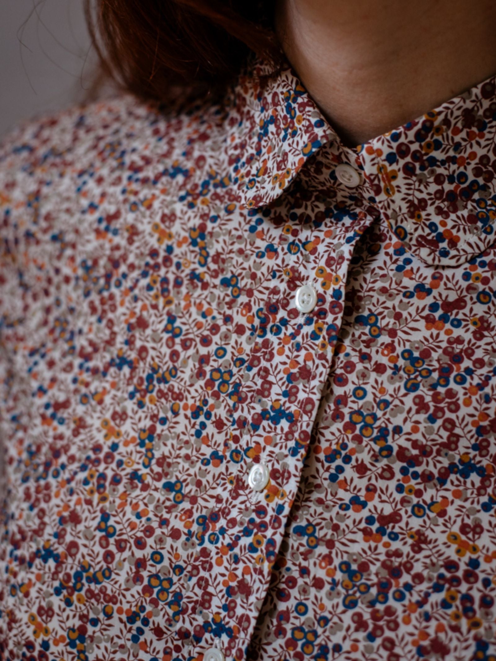 A close-up of a person wearing a buttoned Liberty Print Cotton Shirt by Campbell’s of Beauly, featuring a small, colorful red, blue, and brown floral pattern on fine Tana Lawn cotton. Only the neck, chin, and shoulder are shown.