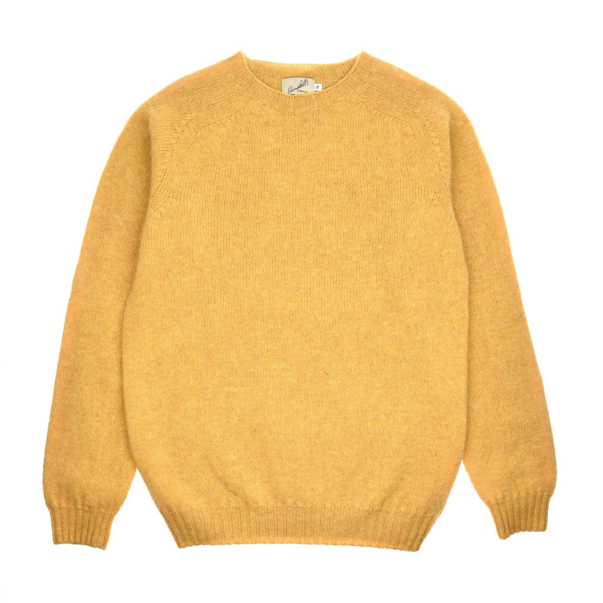 The Campbells of Beauly Shetland Jumper in Honey is a plain, long-sleeved, crew neck knit crafted from soft lambswool yarns with ribbed cuffs, hem, and neckline for classic comfort. Laid flat on a white background.