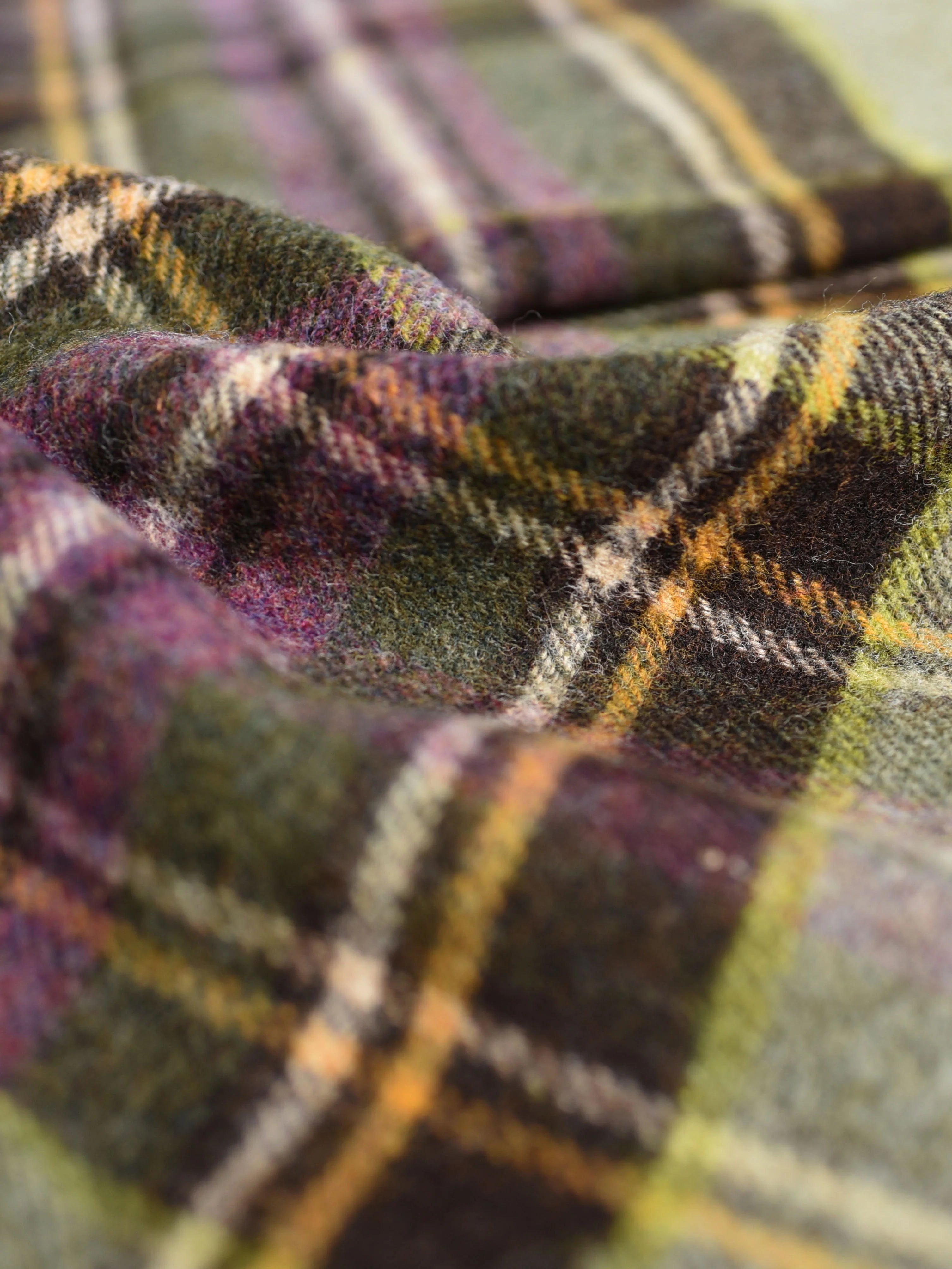 A close-up of the Strathglass Throw by Campbells of Beauly shows its soft lambswool texture and classic tartan pattern in green, yellow, purple, and black, with gentle wrinkles adding warmth and timeless charm.