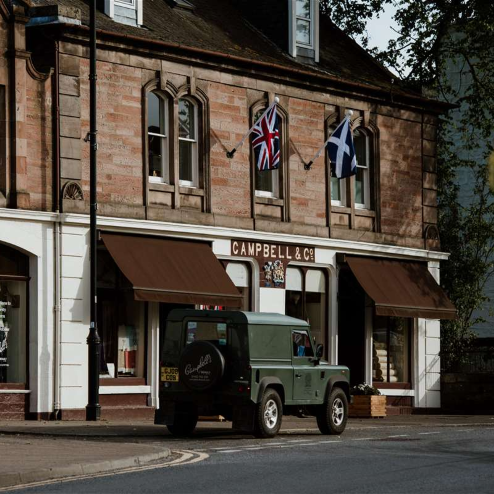 A green Land Rover is parked in front of Campbells of Beauly, a stone building with brown awnings and union jack and Scottish flags above.