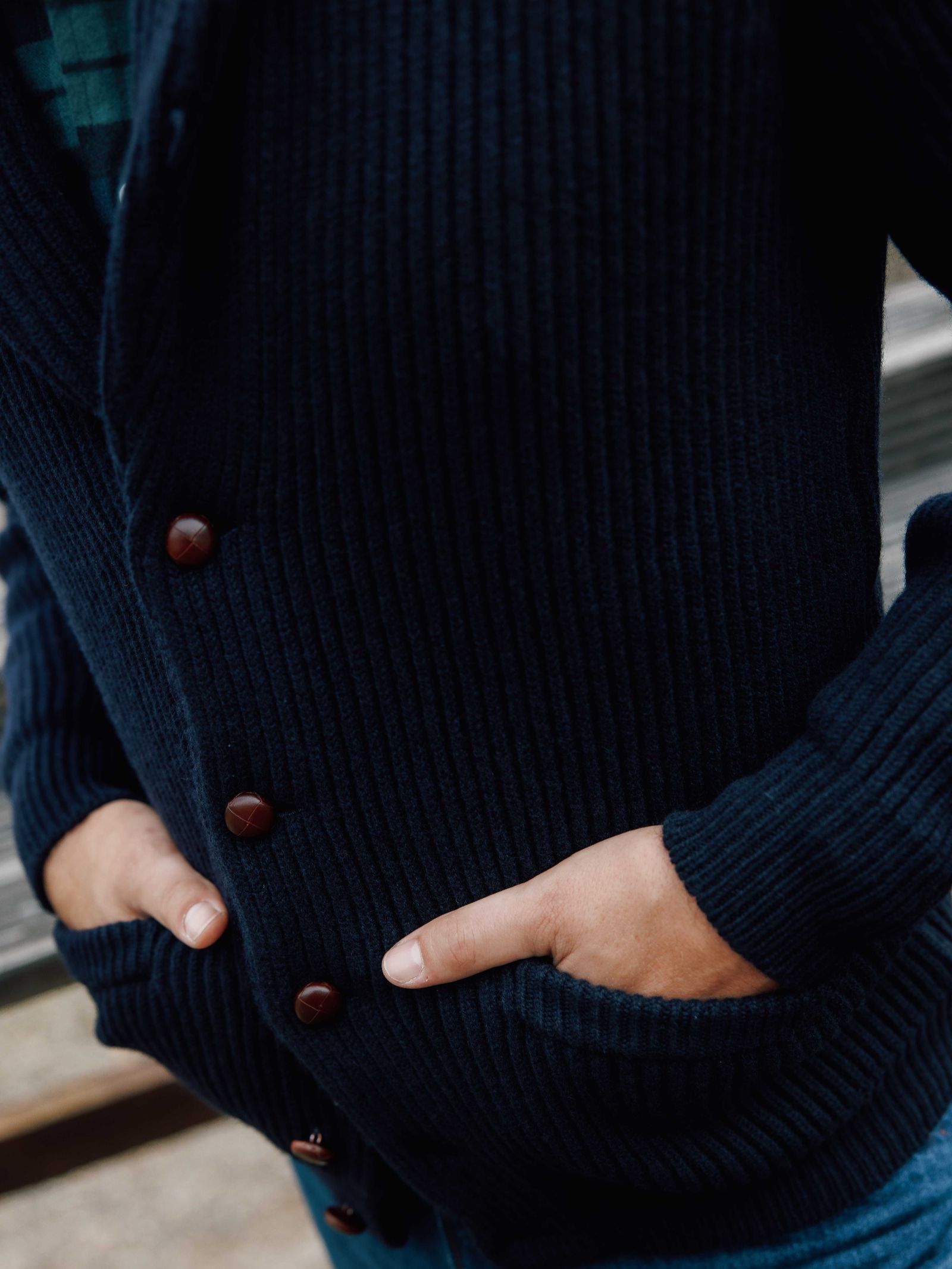 A person wears Campbell's of Beauly Shawl Collar Cardigan in dark blue, featuring a ribbed texture, brown buttons, and pockets. Only their torso and hands are visible, suggesting classic country gentleman style.