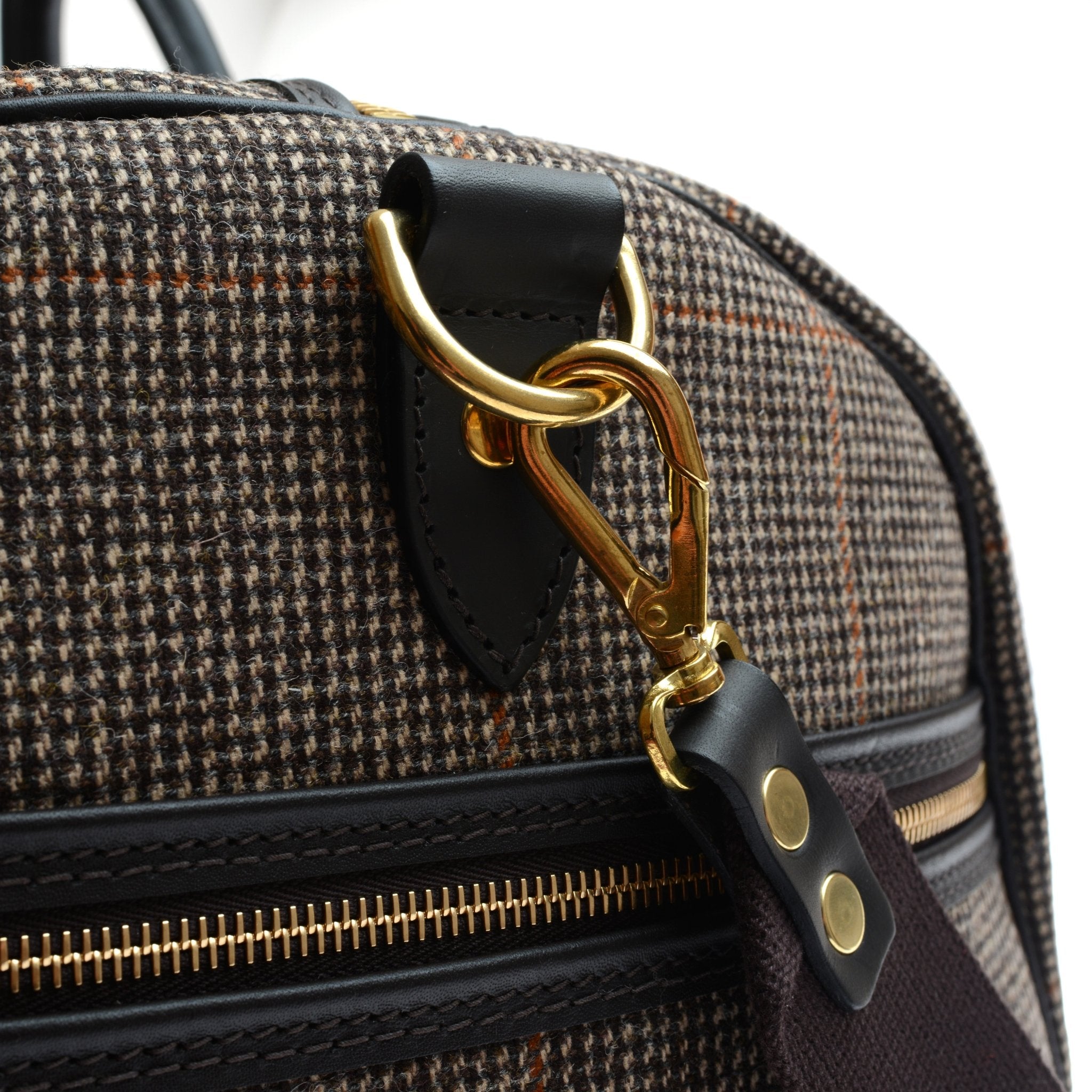 Close-up of the Campbells of Beauly Hand Luggage Holdall, featuring brown plaid fabric with orange lines, a gold zipper and clasp, and bridle leather straps with a ring.