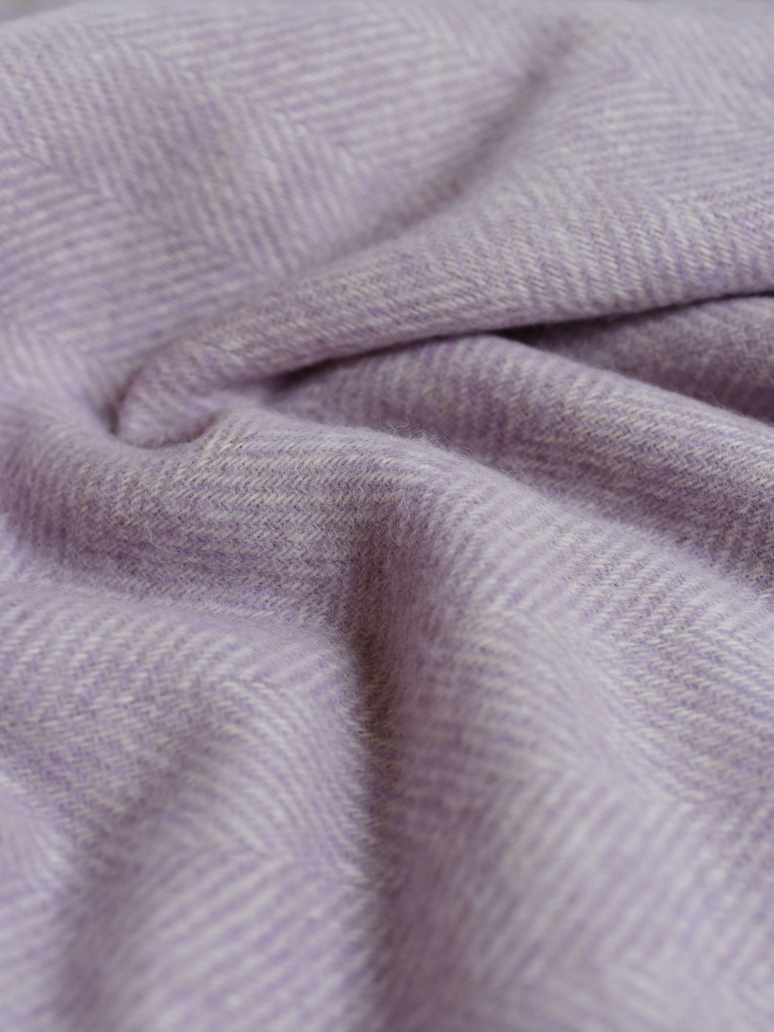 Close-up of the British Wool Throw by Campbells of Beauly, featuring soft light purple wool in a subtle herringbone pattern, gently folded for natural curves and shadows. Expertly woven in Scotland for timeless elegance.