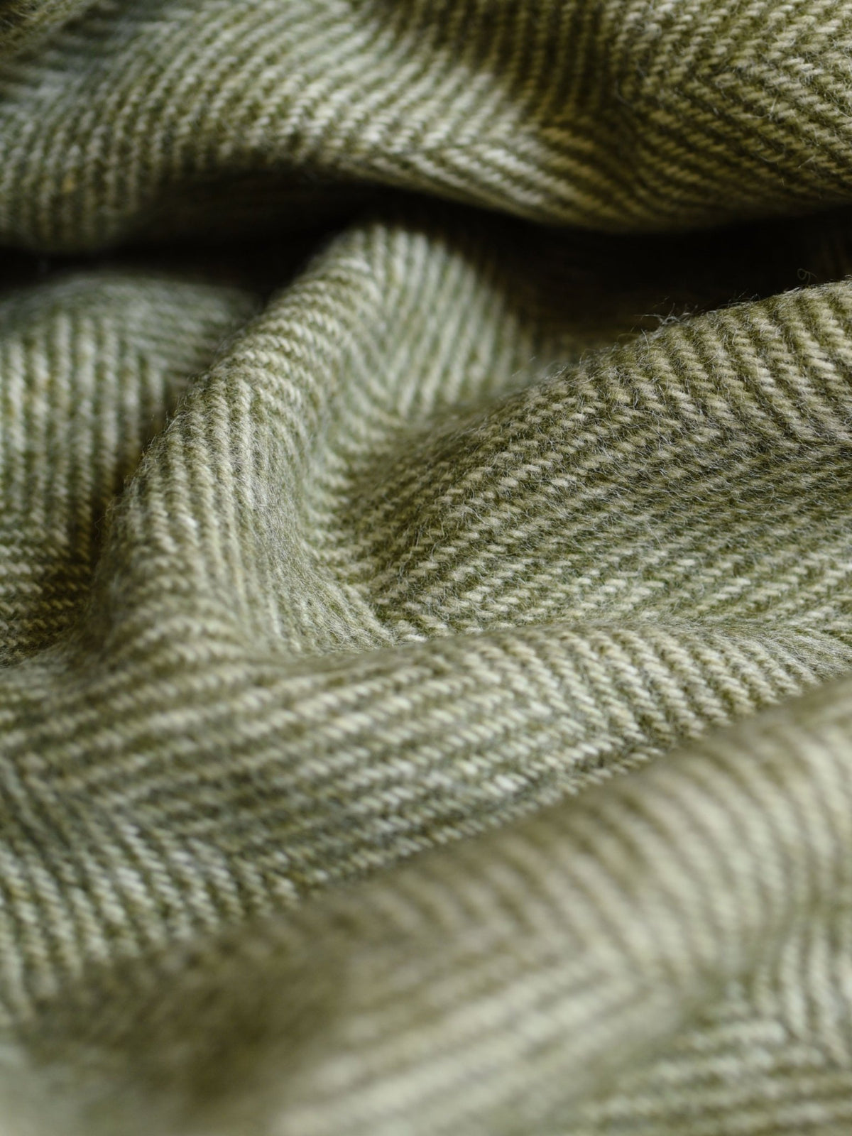 Close-up of green and beige herringbone patterned fabric with soft folds and a textured surface, expertly woven in Scotland by Campbell’s of Beauly for the British Wool Throw Green.