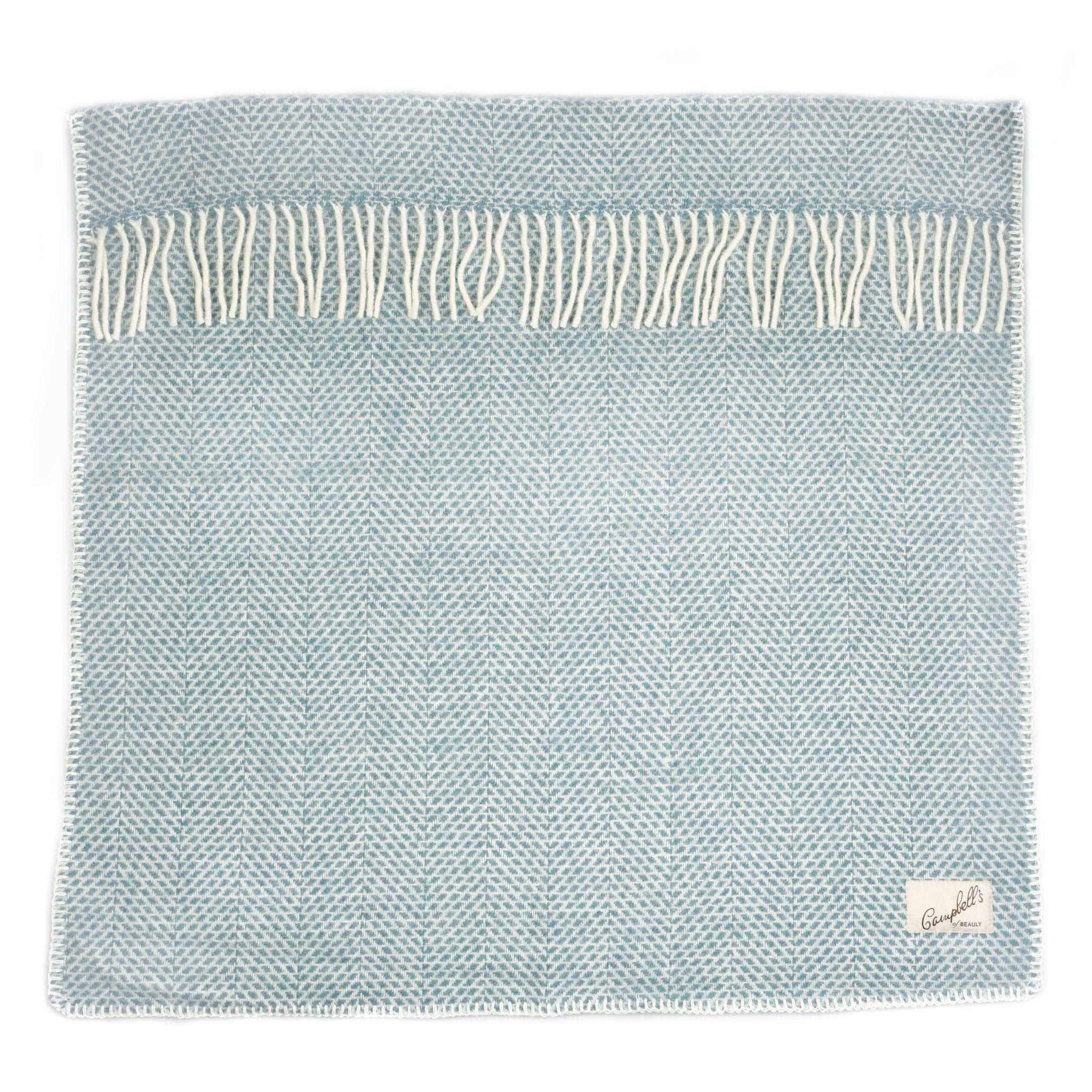 The Campbells of Beauly Baby Blanket is a blue woven piece with a subtle pattern, white fringe on one edge, and a small fabric label in one corner. Its soft weave ensures year-round comfort, ideal as a wool pram blanket.