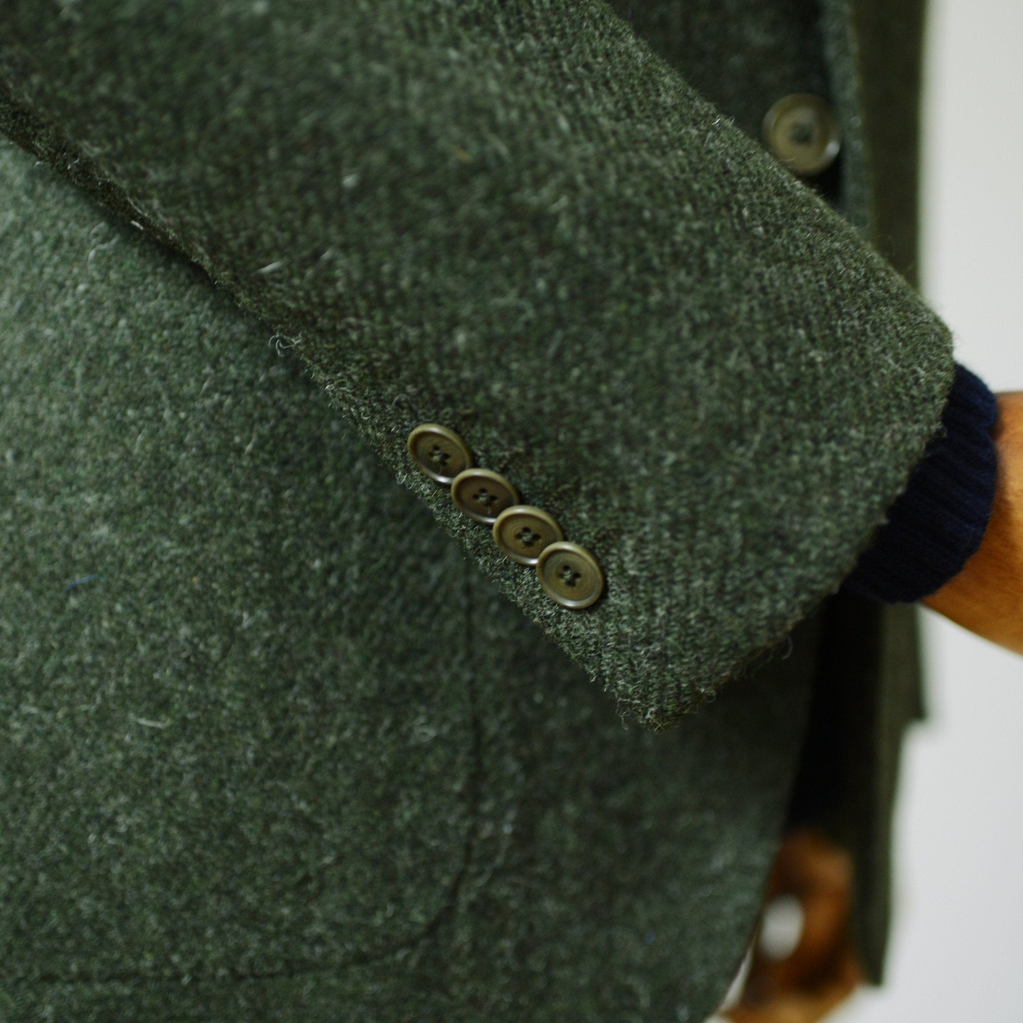 Close-up of a green Campbells of Beauly Harris Tweed Jacket sleeve, showing four brown cuff buttons and a dark blue sweater at the wrist.
