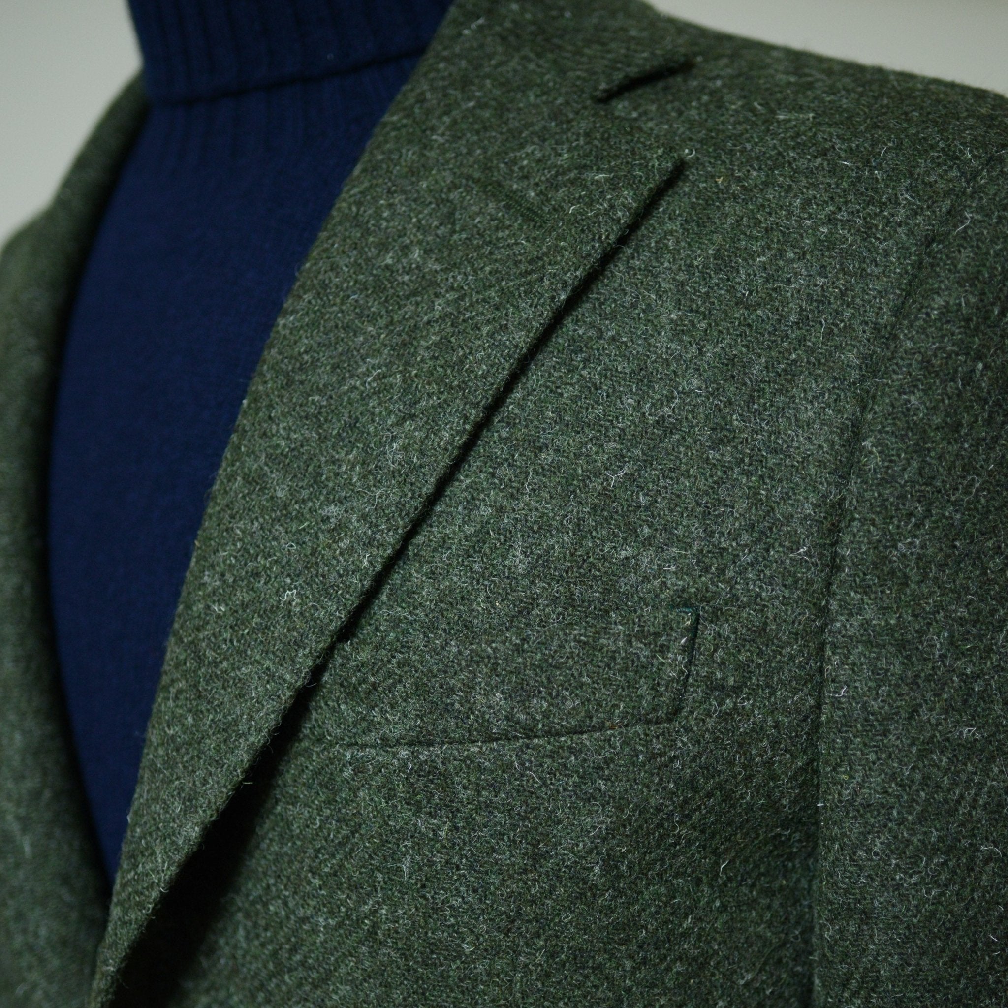 Close-up of a person wearing the Campbells of Beauly Harris Tweed Jacket over a navy blue turtleneck, focusing on the lapel and chest pocket. The neutral, blurred background highlights the jacket’s tailored design.
