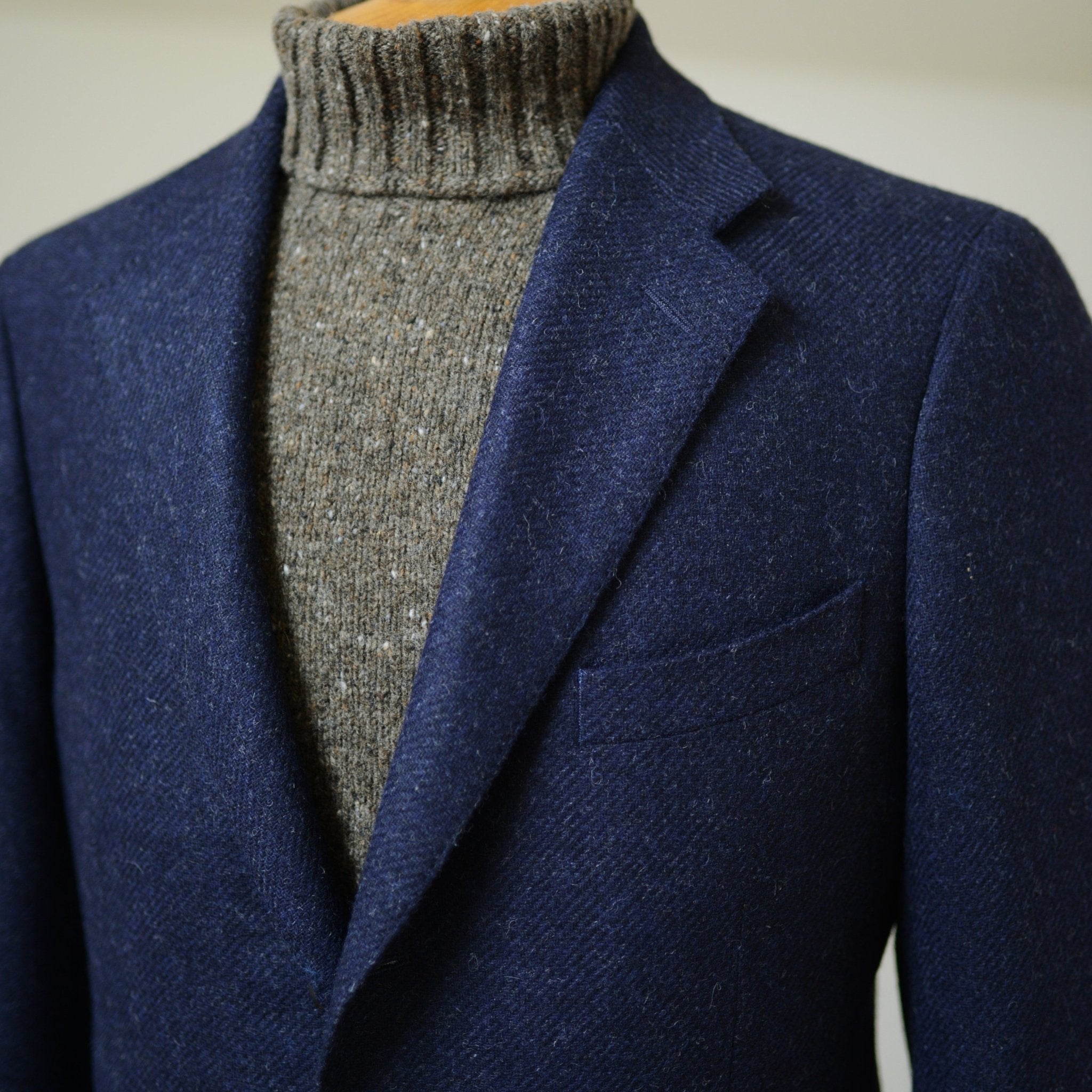 A close-up of a person wearing a Campbells of Beauly Navy Twill House Jacket over a thick gray knitted turtleneck. The formal and stylish outfit shows only the torso and neck.