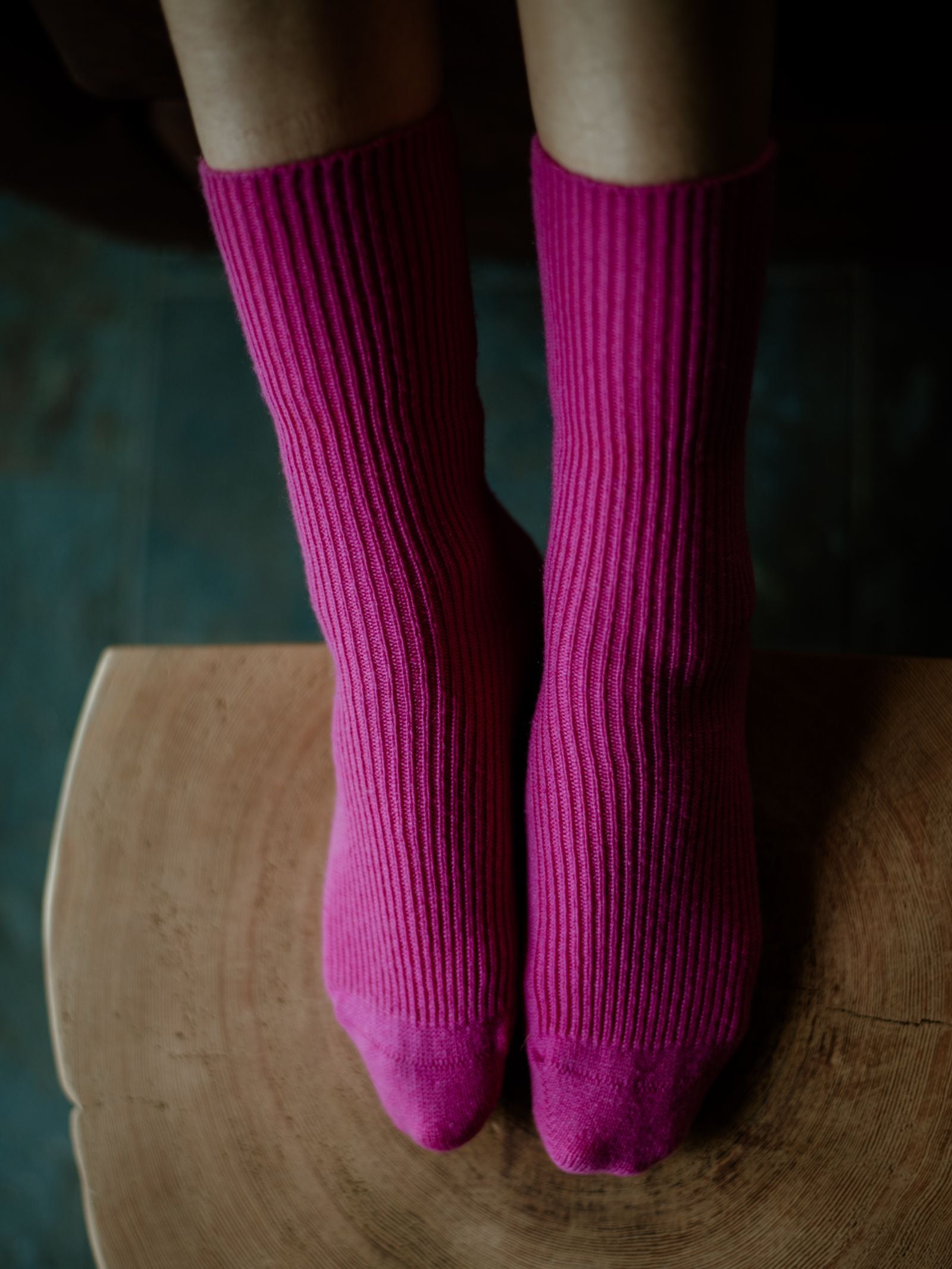 A close-up of two feet in Campbells of Beauly Plain Cashmere Socks—bright pink and ribbed—rest on wood, showcasing a touch of luxury gift elegance.