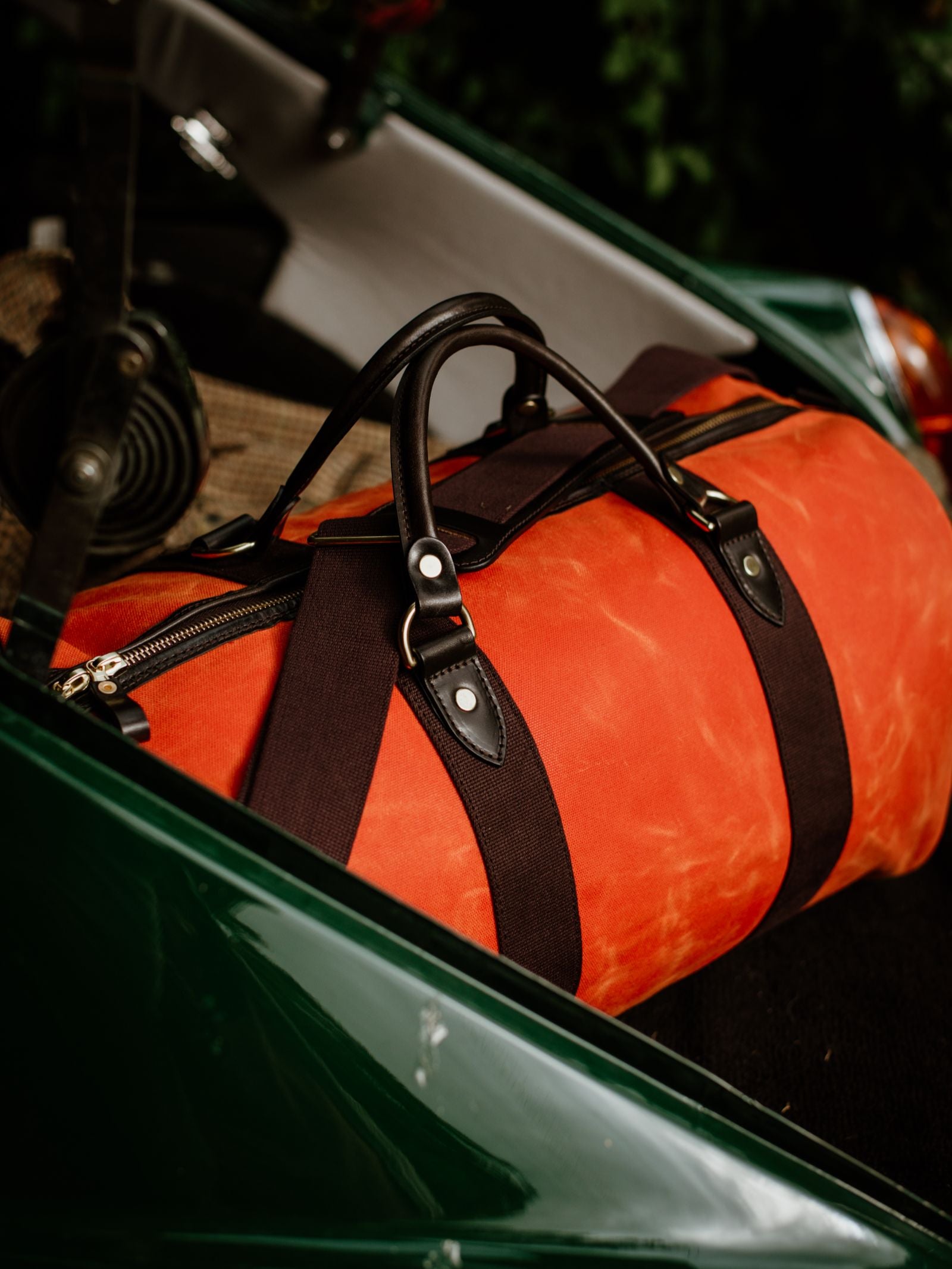 A Campbell's of Beauly Wax Holdall, featuring black bridle leather handles, rests on the seat of a green vintage car.