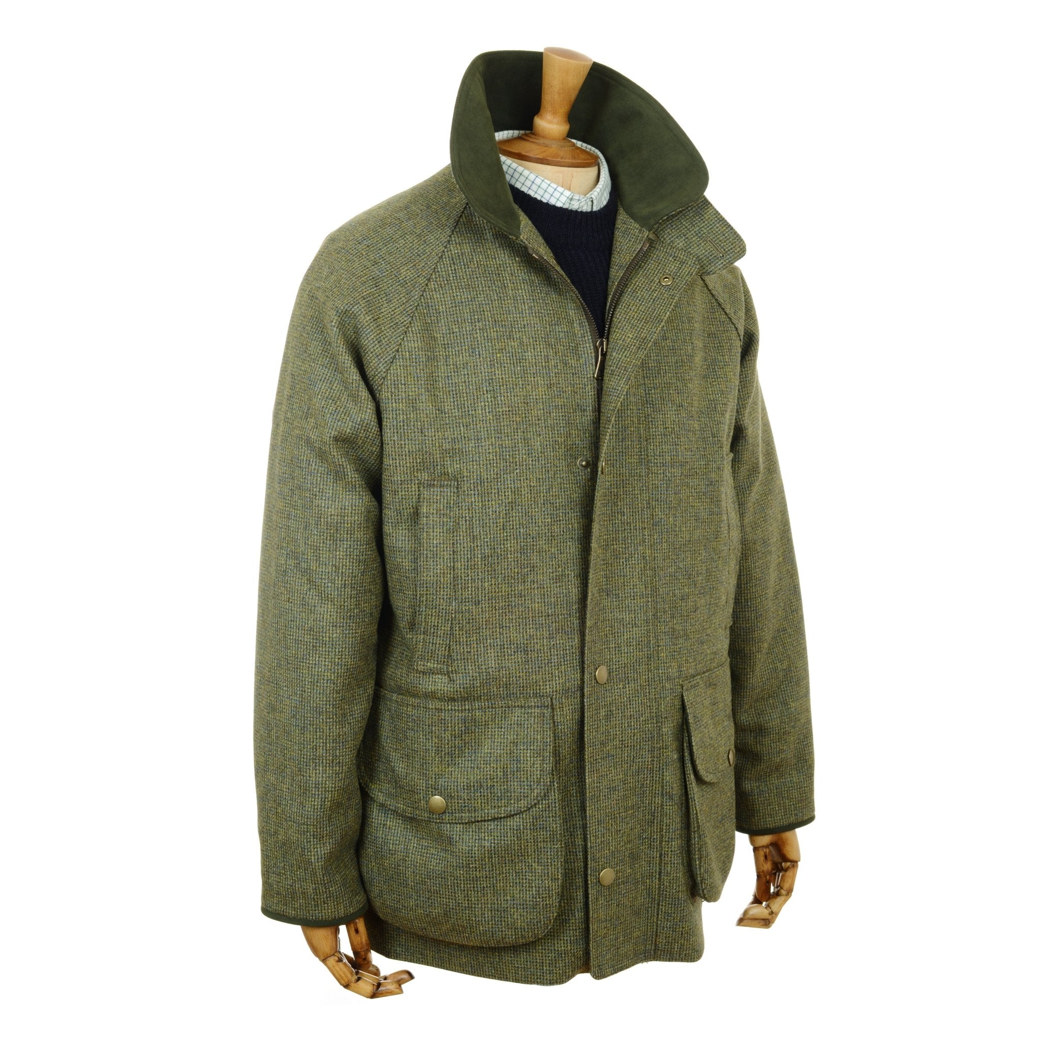 Campbells of Beauly Tweed Field Coat in green, featuring a high Alcantara collar and two large front pockets, is shown on a wooden mannequin dressed in a light sweater and dark shirt.