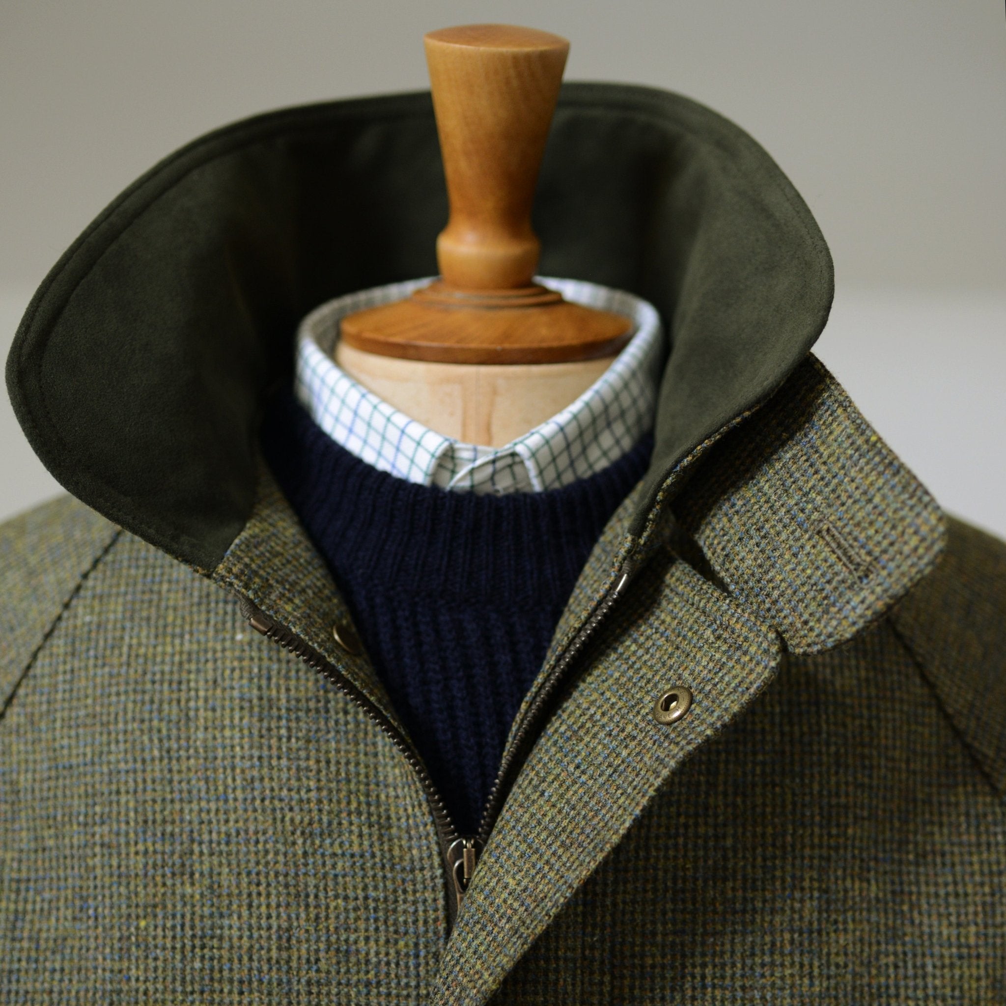 A mannequin wears Campbells of Beauly Tweed Field Coat, its high collar turned up to reveal the Alcantara inner lining and button details, layered over a navy sweater and white checkered shirt.