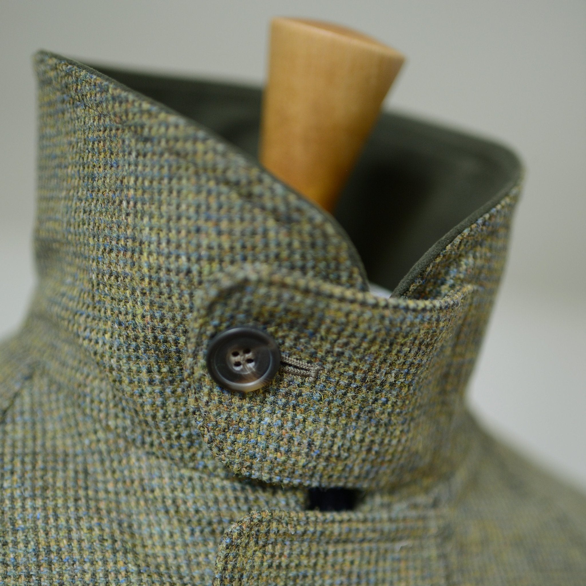 Close-up of Campbells of Beauly Tweed Field Coat—this men’s jacket features a high collar with a single dark button, crafted from green and brown check tweed, shown on a wooden mannequin.