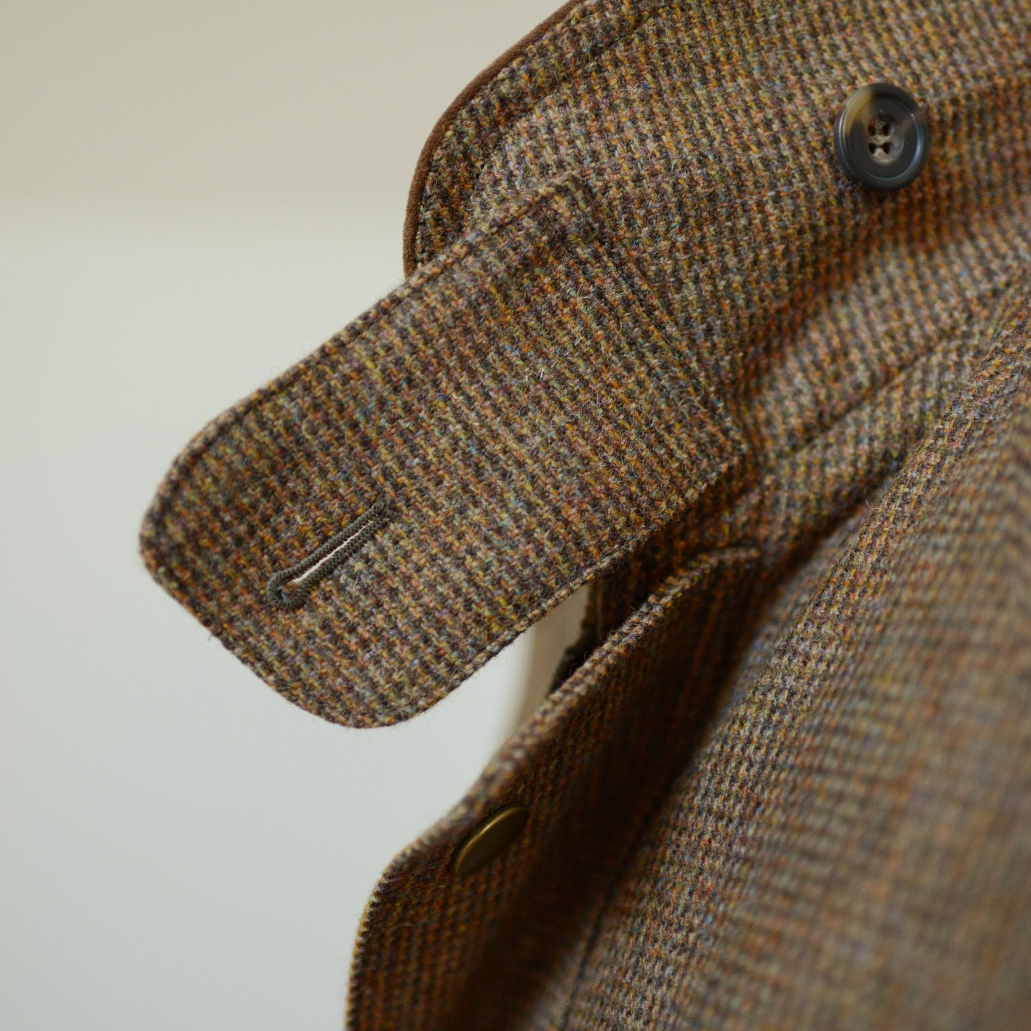 Close-up of Campbells of Beauly Tweed Field Coat showcasing the brown textured tweed fabric, strap and buttonhole detail, precise stitching, and an Alcantara collar for added style.