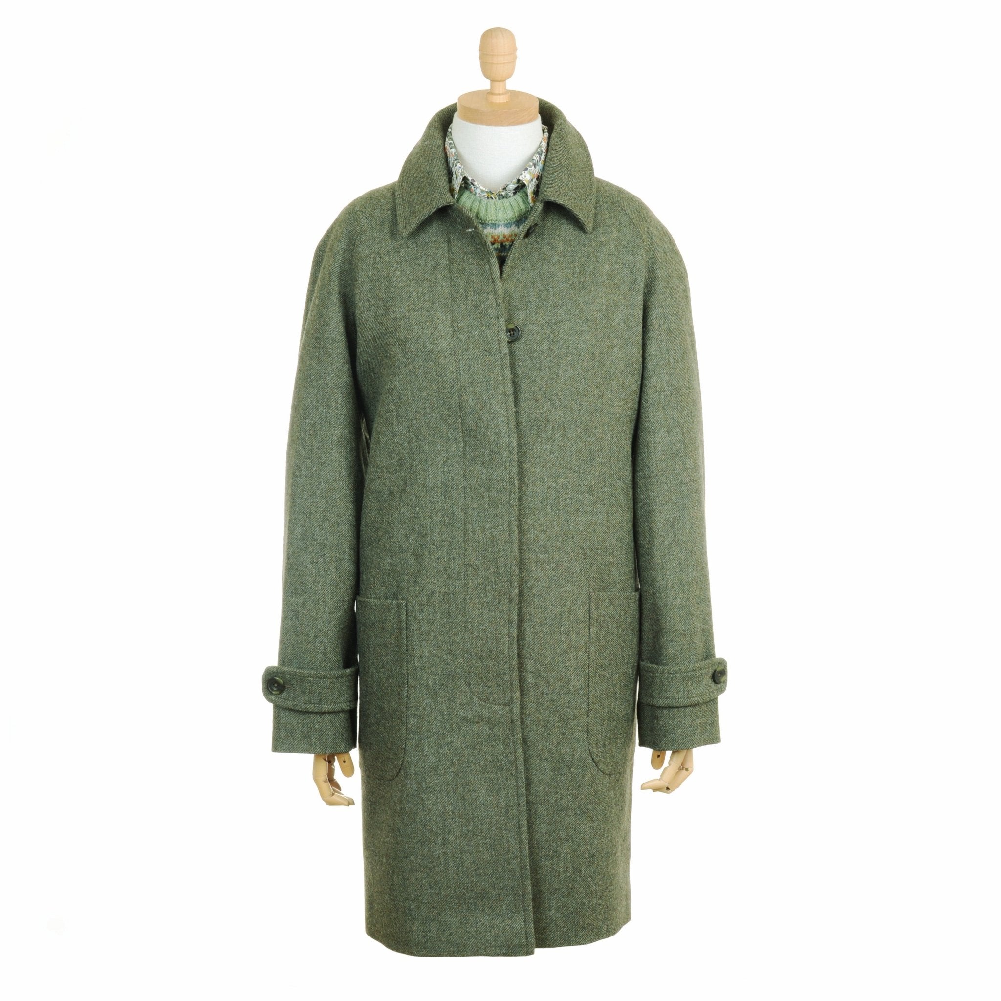 A mannequin models Campbells of Beauly Heath Collar Coat—a long green wool design with front pockets, buttoned cuffs, and single-breasted front—layered over a patterned knit for a stylish, modern everyday look.