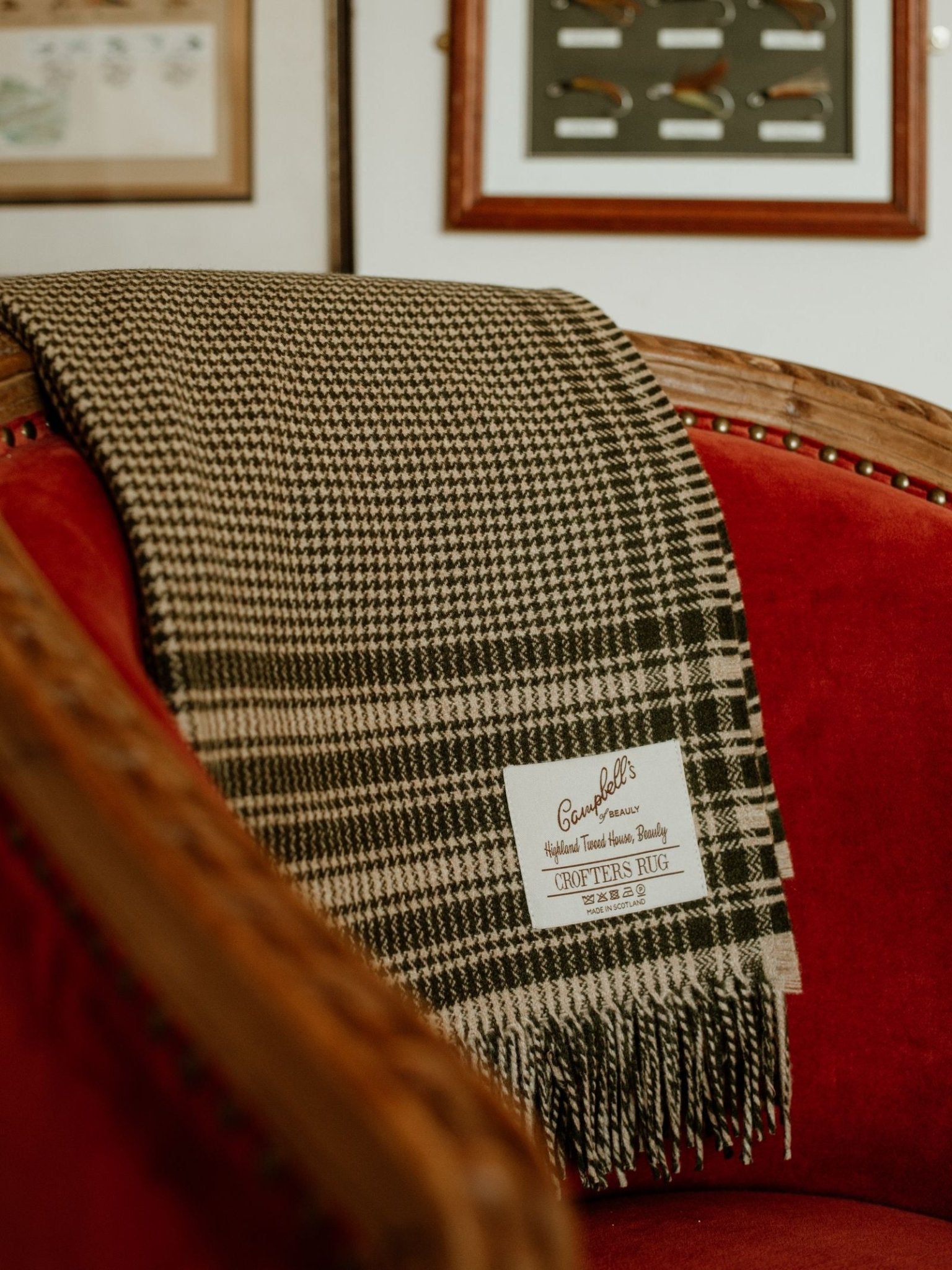 A black and white houndstooth Crofters Blanket by Campbell's of Beauly is draped over a vintage red velvet chair. Framed art on the wall enhances the country-inspired setting.