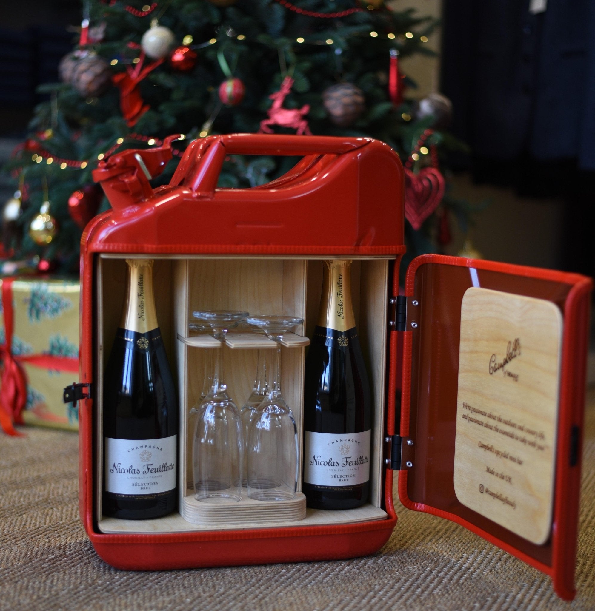 The Brimoncourt Champagne Upcycled Mini Bar by Campbells of Beauly transforms a Jerry can into a unique bar with compartments for two bottles of Brimoncourt champagne and two flutes, set beside a festive Christmas tree and wrapped gift.