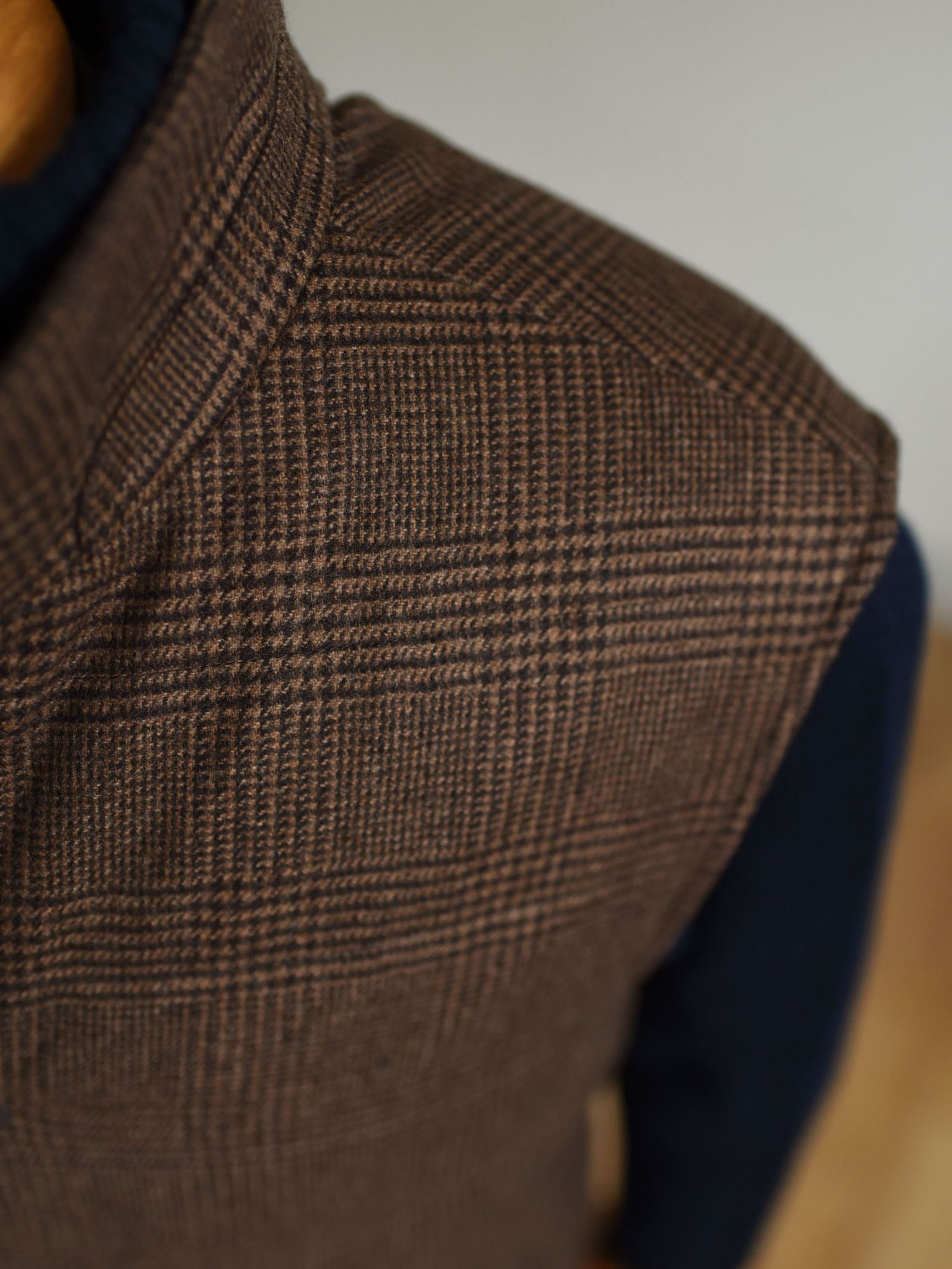Close-up of a persons upper body wearing the Campbells of Beauly Cashmere Gun Club Quilted Gilet over a dark navy sweater, set against a blurred neutral background.