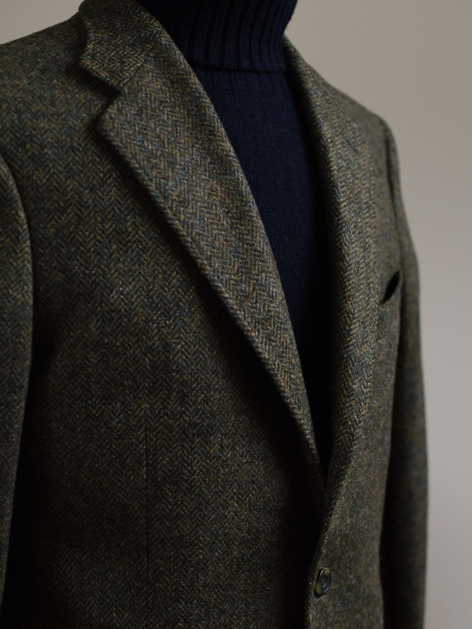 A close-up shows a person wearing the Campbell's of Beauly Green Herringbone House Jacket over a black turtleneck, pictured from the chest up against a neutral background.