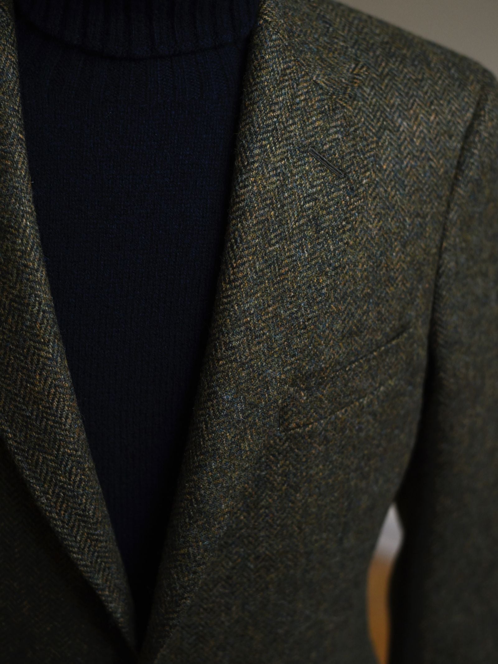Close-up of a person in the Campbells of Beauly Green Herringbone House Jacket over a black or navy ribbed turtleneck, showcasing the rich texture and timeless pattern of this classic tweed blazer.