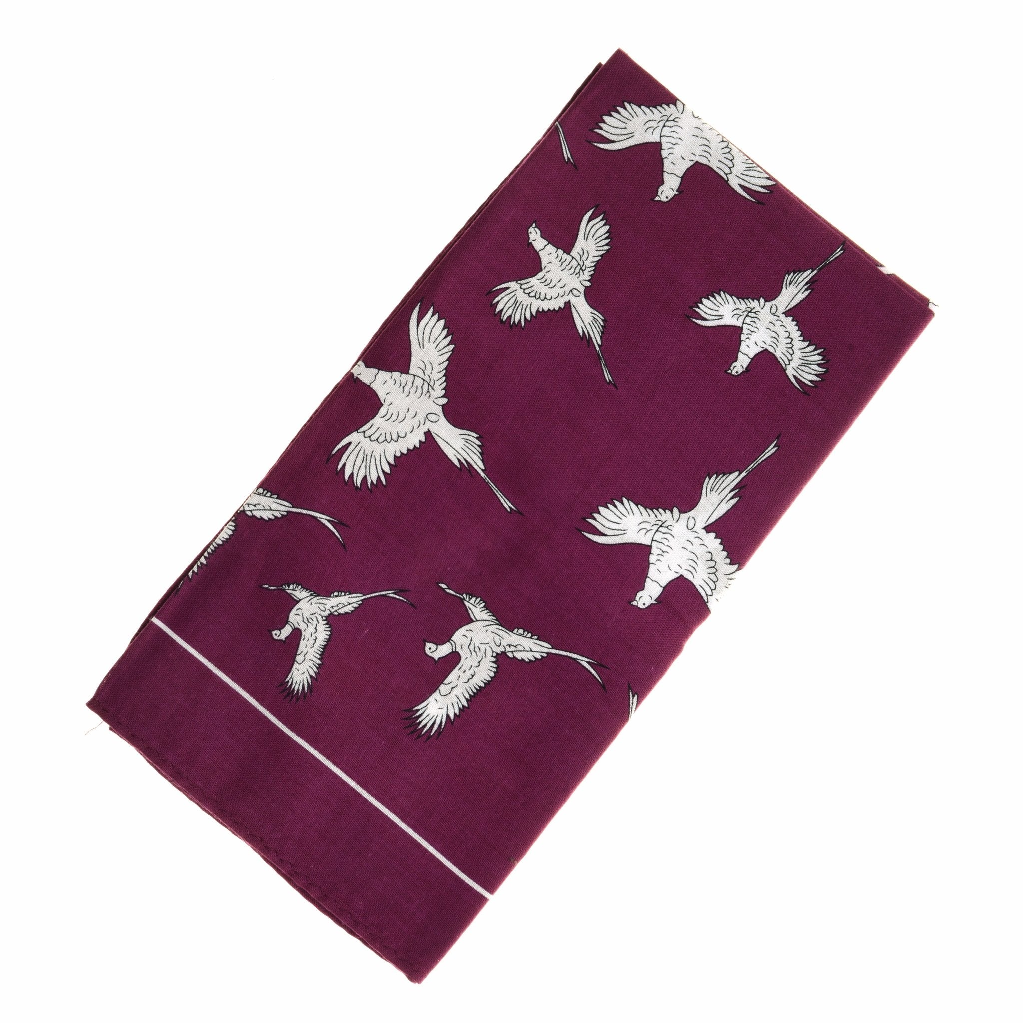 The Cotton Pheasant Hank by Campbells of Beauly is a purple cotton handkerchief adorned with white cranes in flight, combining versatility and style.