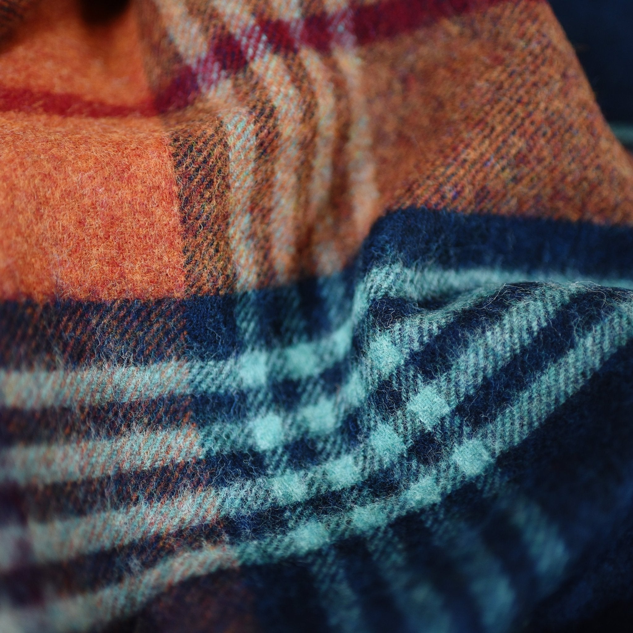 Close-up of the Torgormack Lambswool Throw by Campbells of Beauly, featuring a cosy plaid pattern in orange, blue, teal, and burgundy with soft, textured folds—bringing Yorkshire-inspired warmth to your home.