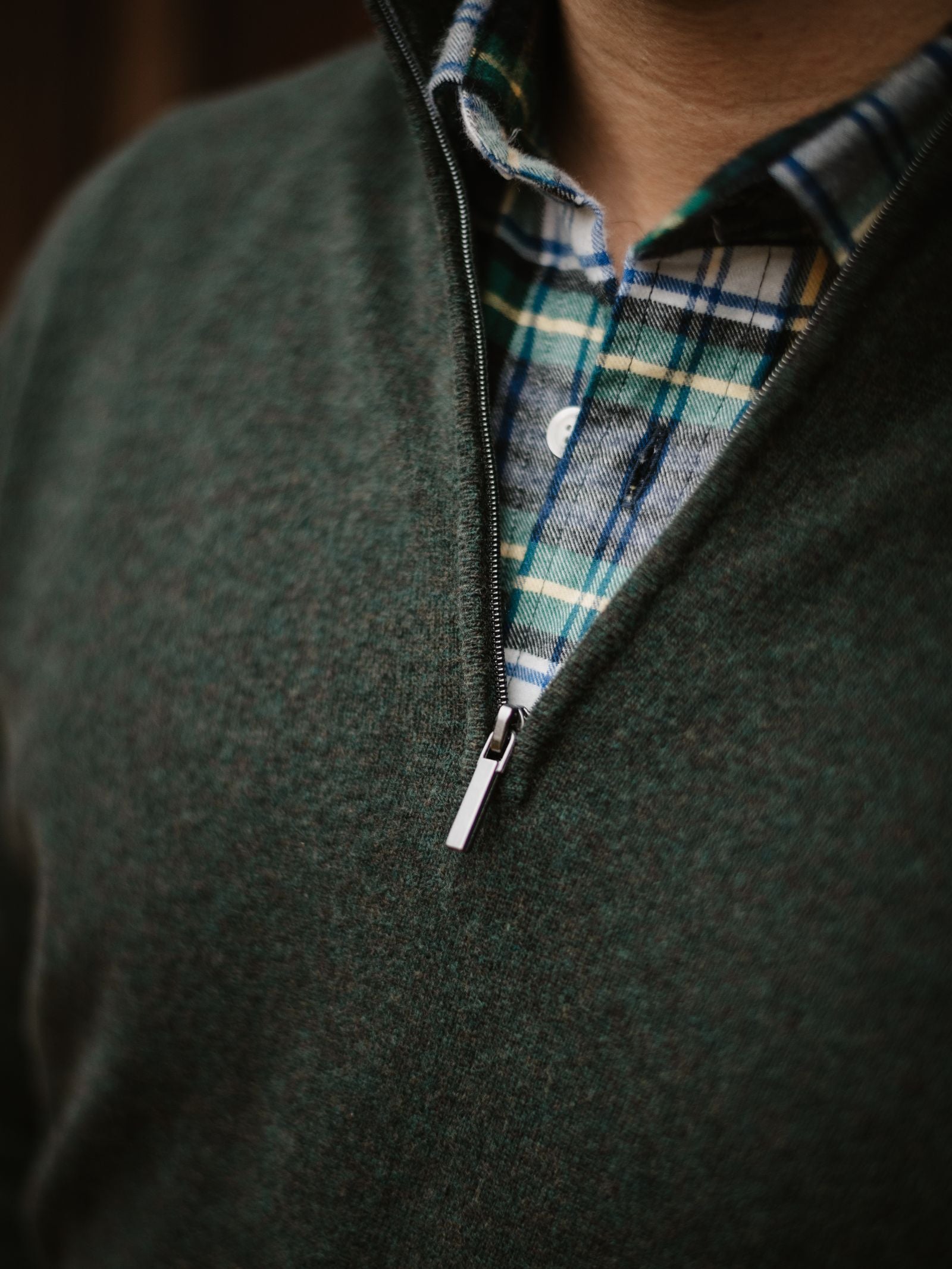 Close-up of a person in a Campbell’s of Beauly Merino & Cashmere Quarter Zip Jumper over a blue, green, and white plaid button-up shirt. The zip is partly open, showing the shirt's collar and top buttons.