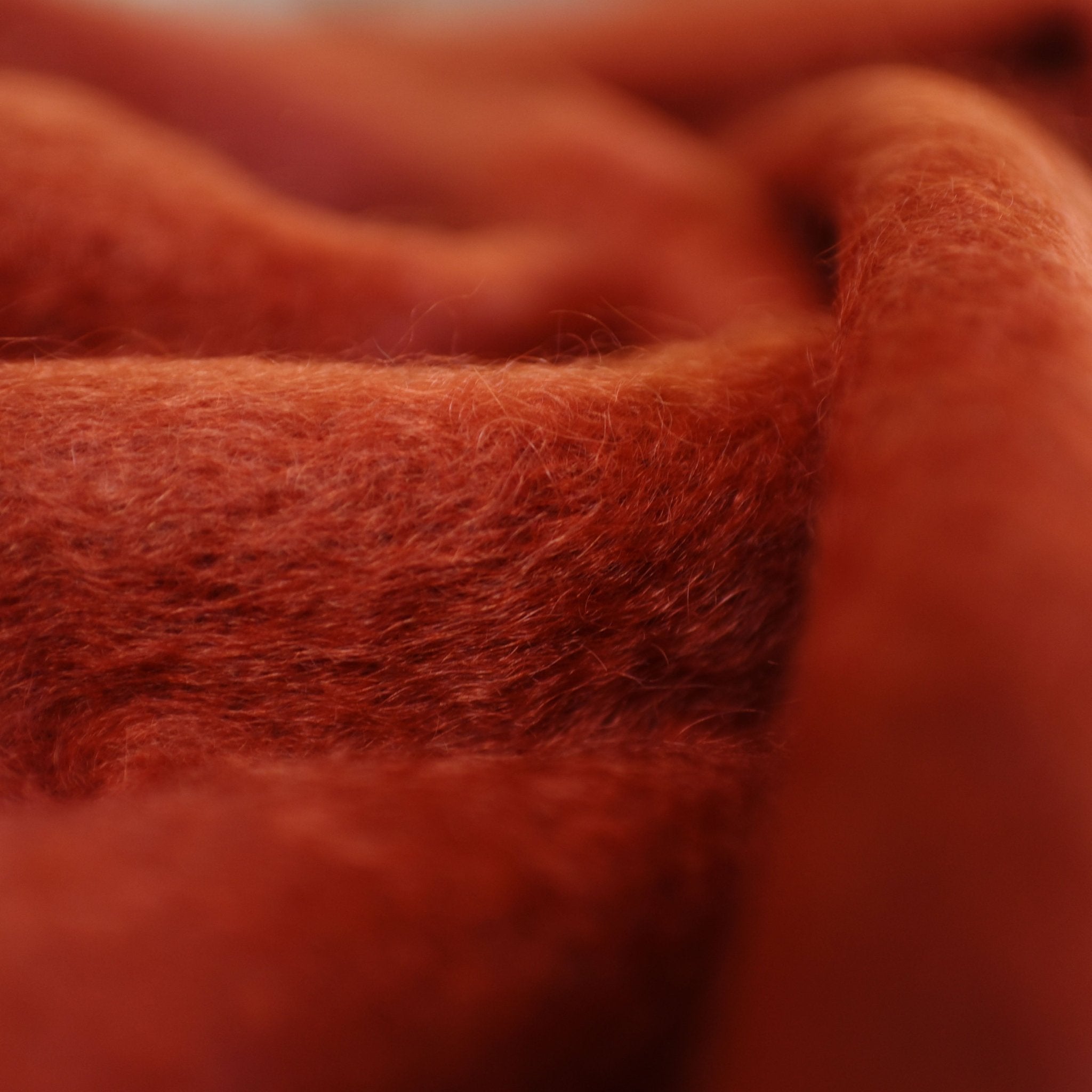 Close-up of a soft, fuzzy red-orange Mohair Throw by Campbells of Beauly, featuring a textured, fluffy surface and gentle folds—a luxurious, cozy layer ideal for any Yorkshire-inspired space.