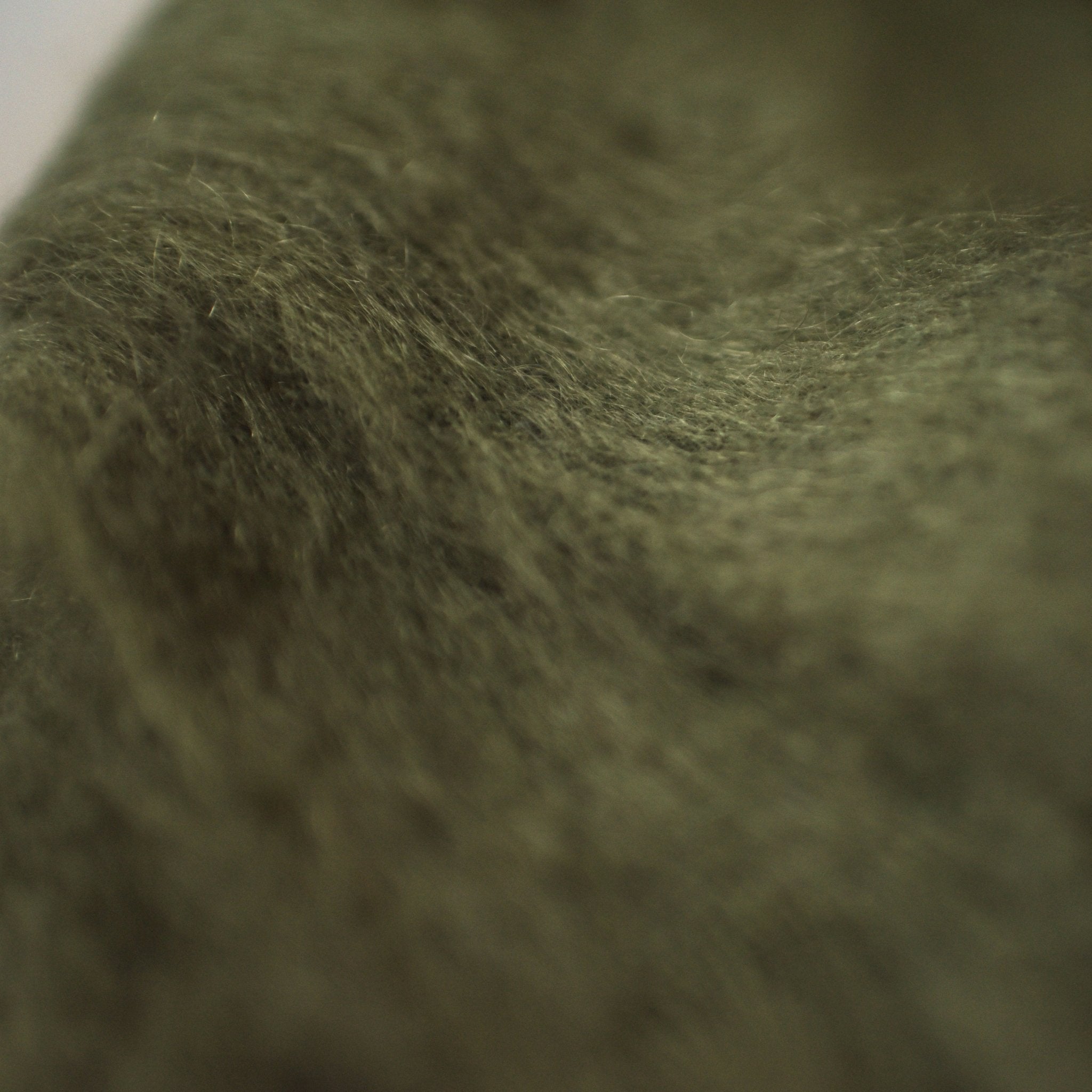 Close-up image of the Campbells of Beauly Mohair Throw, showcasing its soft, fuzzy green texture and gentle folds. Lighting highlights the luxurious material with subtle shadows across its surface.