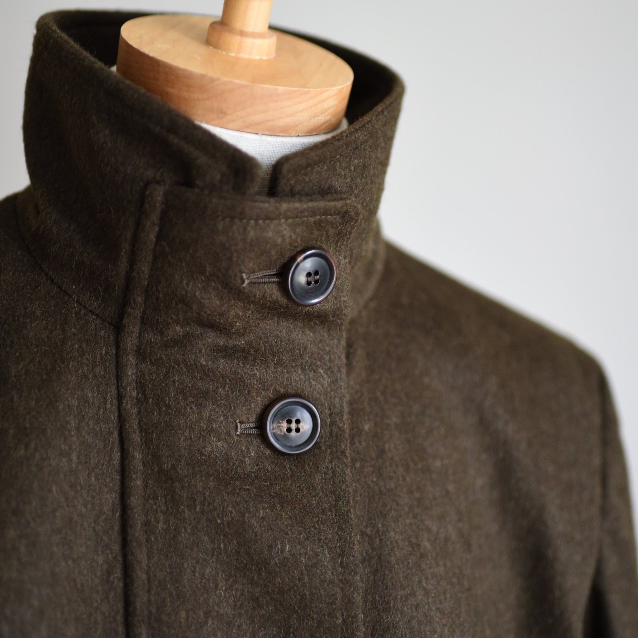 Close-up of the Loden Green Field Coat by Campbells of Beauly, crafted from Austrian Loden fabric with a high collar and two black buttons—timeless outerwear showcased on a mannequin against a plain background.