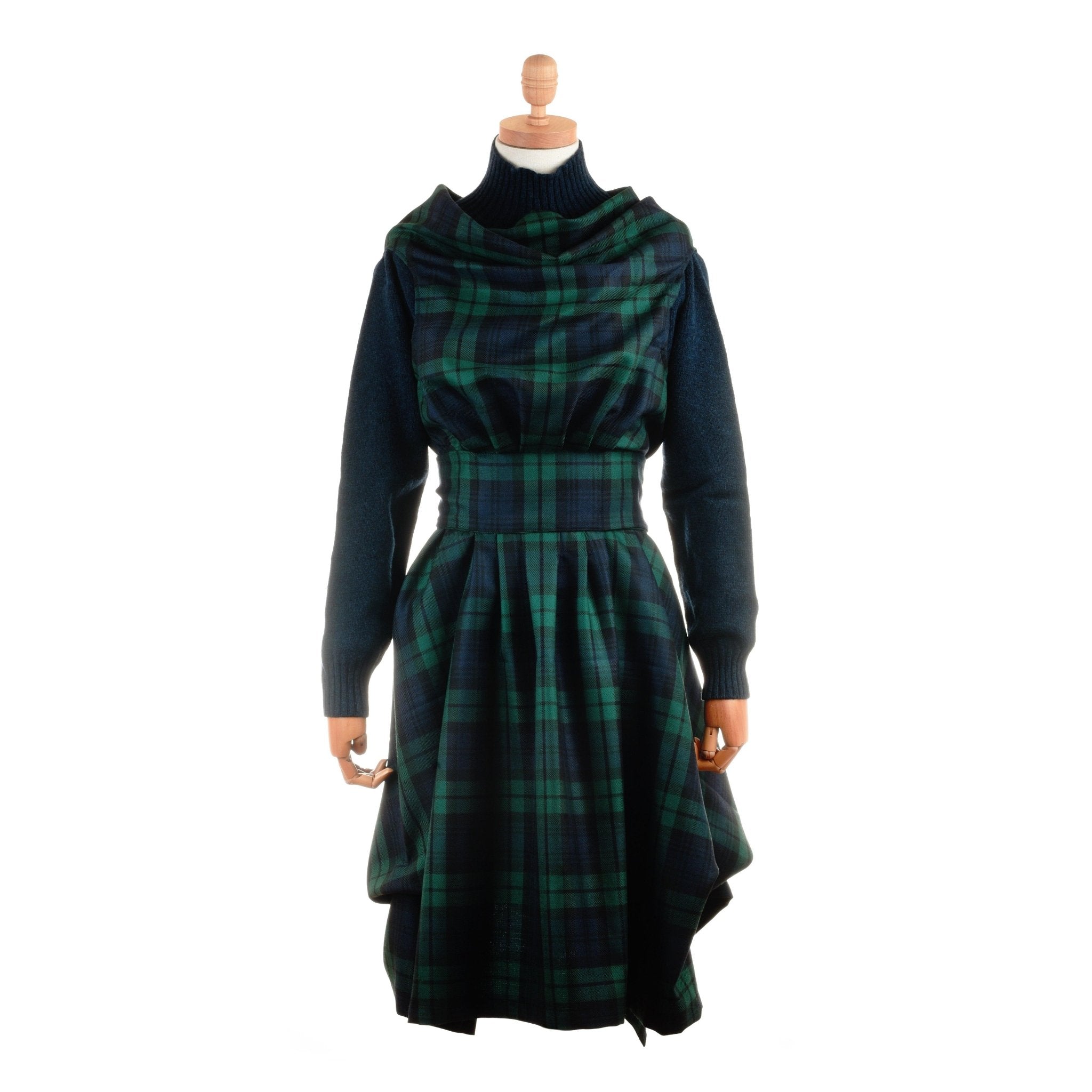 A Campbells of Beauly dressmaker’s mannequin displays a Reversible Wool Wrap Dress in dark green and blue tartan with a fitted waist, long sleeves, draped neckline, and asymmetrical hem against a white background.