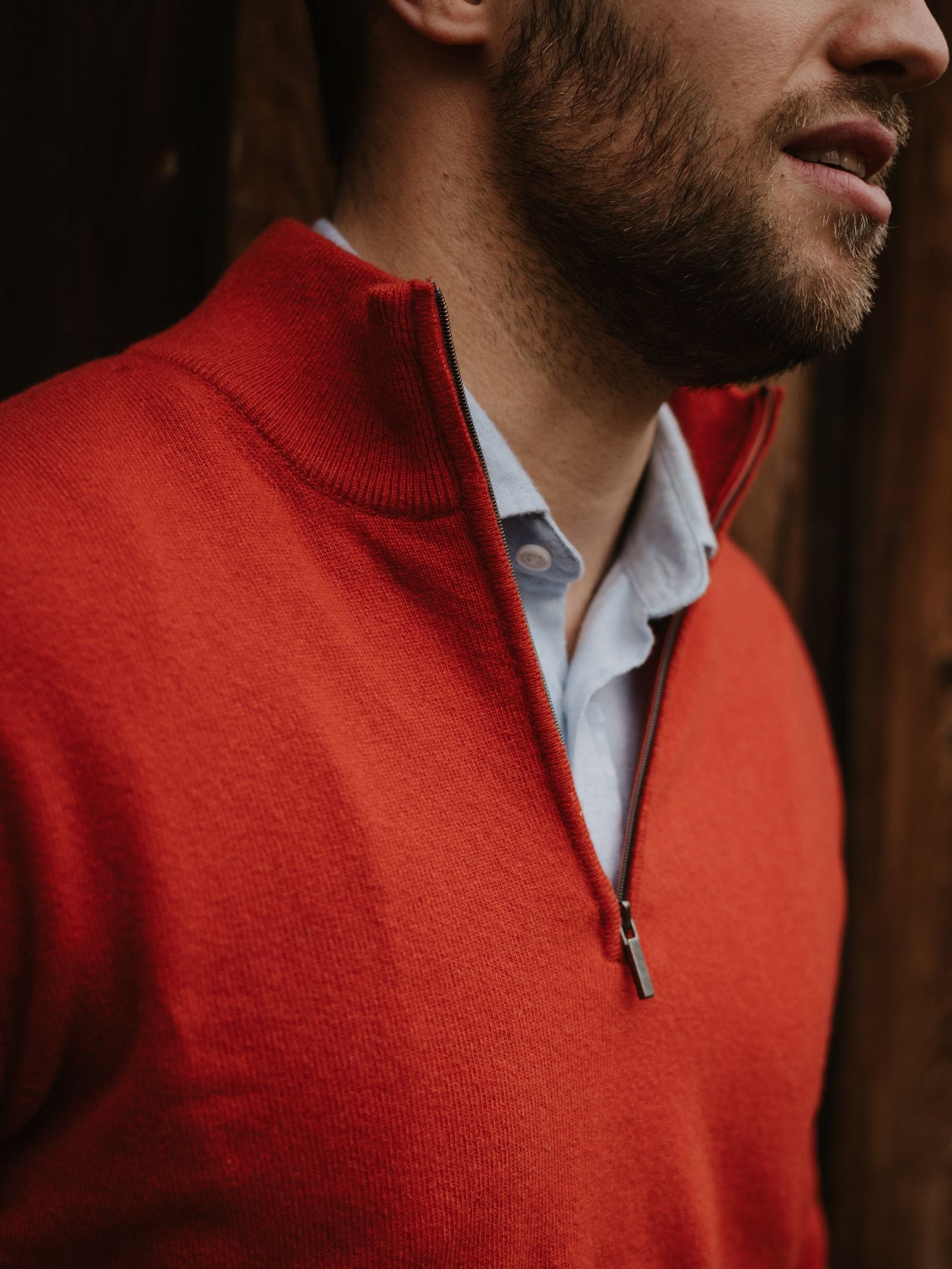 A bearded man wears a light blue collared shirt under the Campbell's of Beauly Merino & Cashmere Quarter Zip Jumper, standing before a wooden wall. The photo captures his upper torso and face in partial profile.