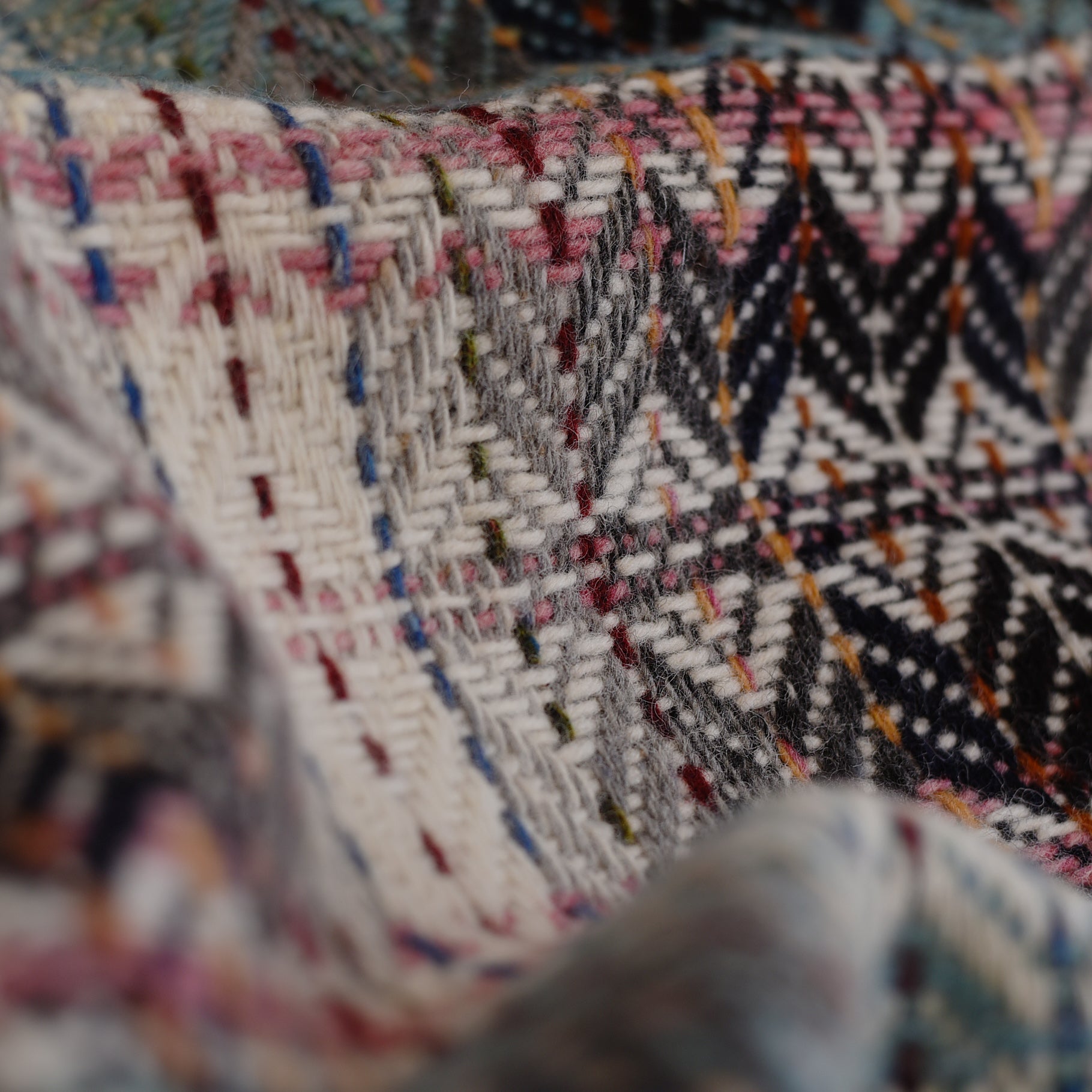 Close-up of the Wyvis Lambswool Throw by Campbells of Beauly, showcasing colorful diamond weave patterns in white, black, pink, blue, and yellow threads with soft fabric folds for beautiful texture.