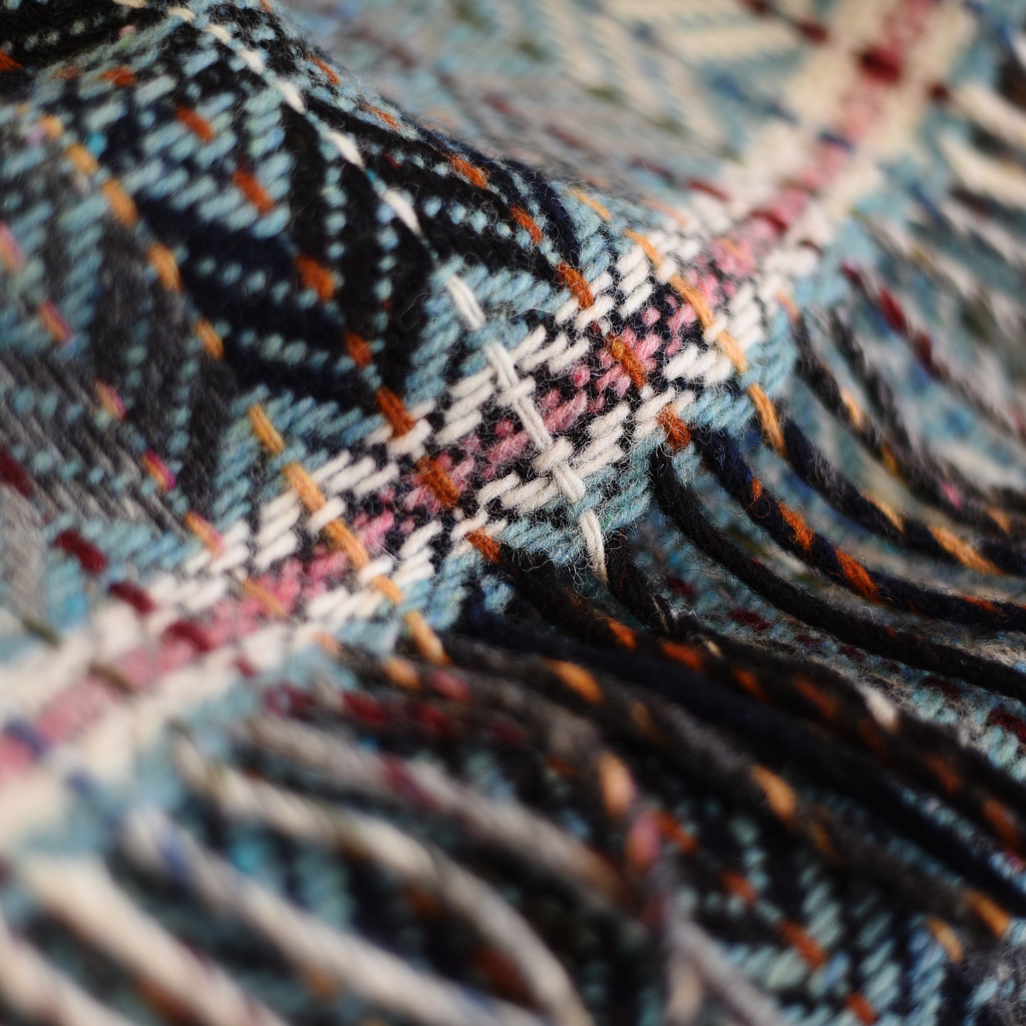 Close-up of the Wyvis Lambswool Throw by Campbells of Beauly, showcasing colorful flecked yarns in blue, orange, pink, and white in a traditional diamond weave with intricate patterns and fringe edges.