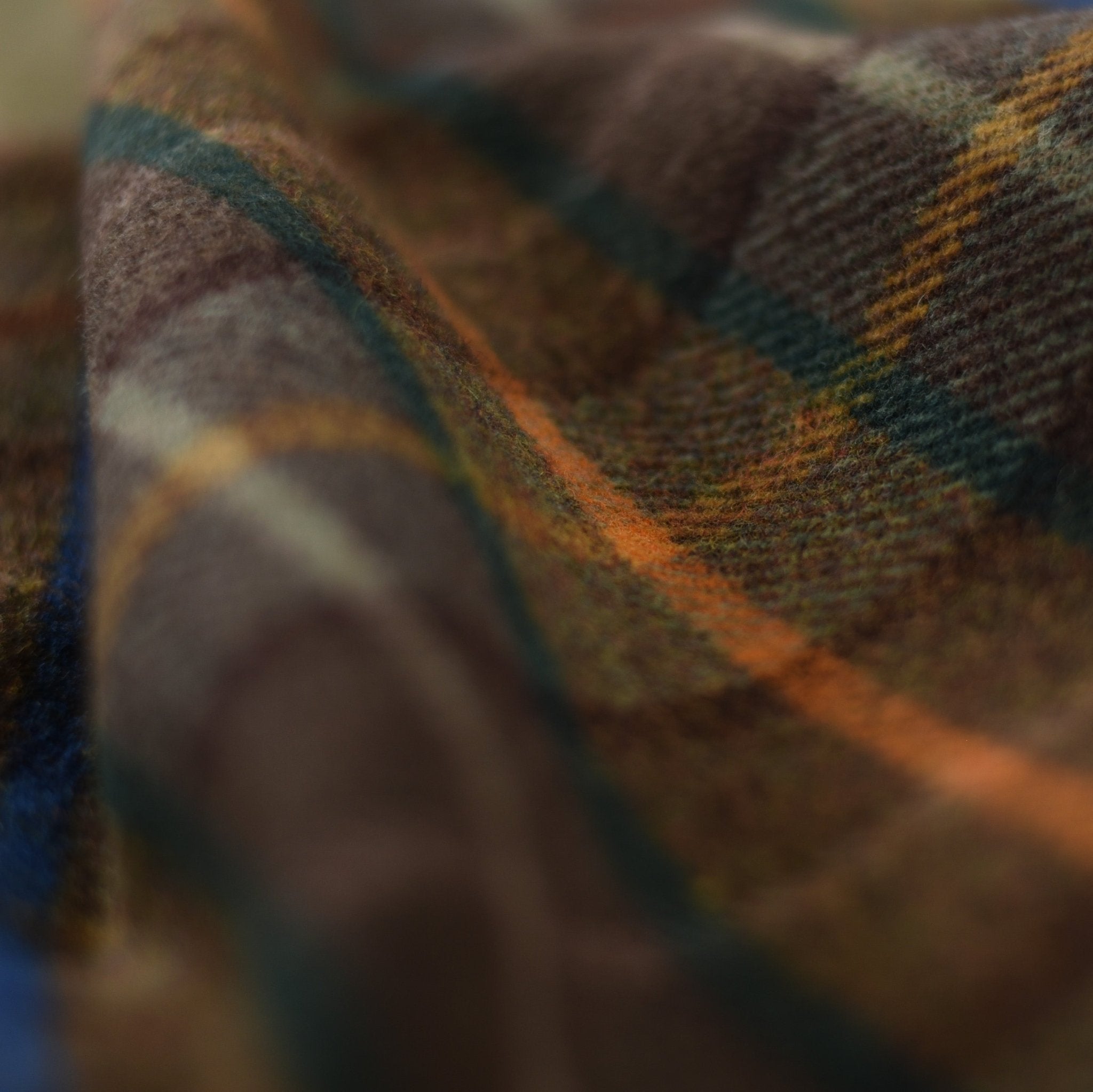 A close-up of Campbells of Beauly Lavender Throw, showcasing its soft lambswool in a plaid pattern with brown, green, orange, and blue tones inspired by the Scottish Borders.