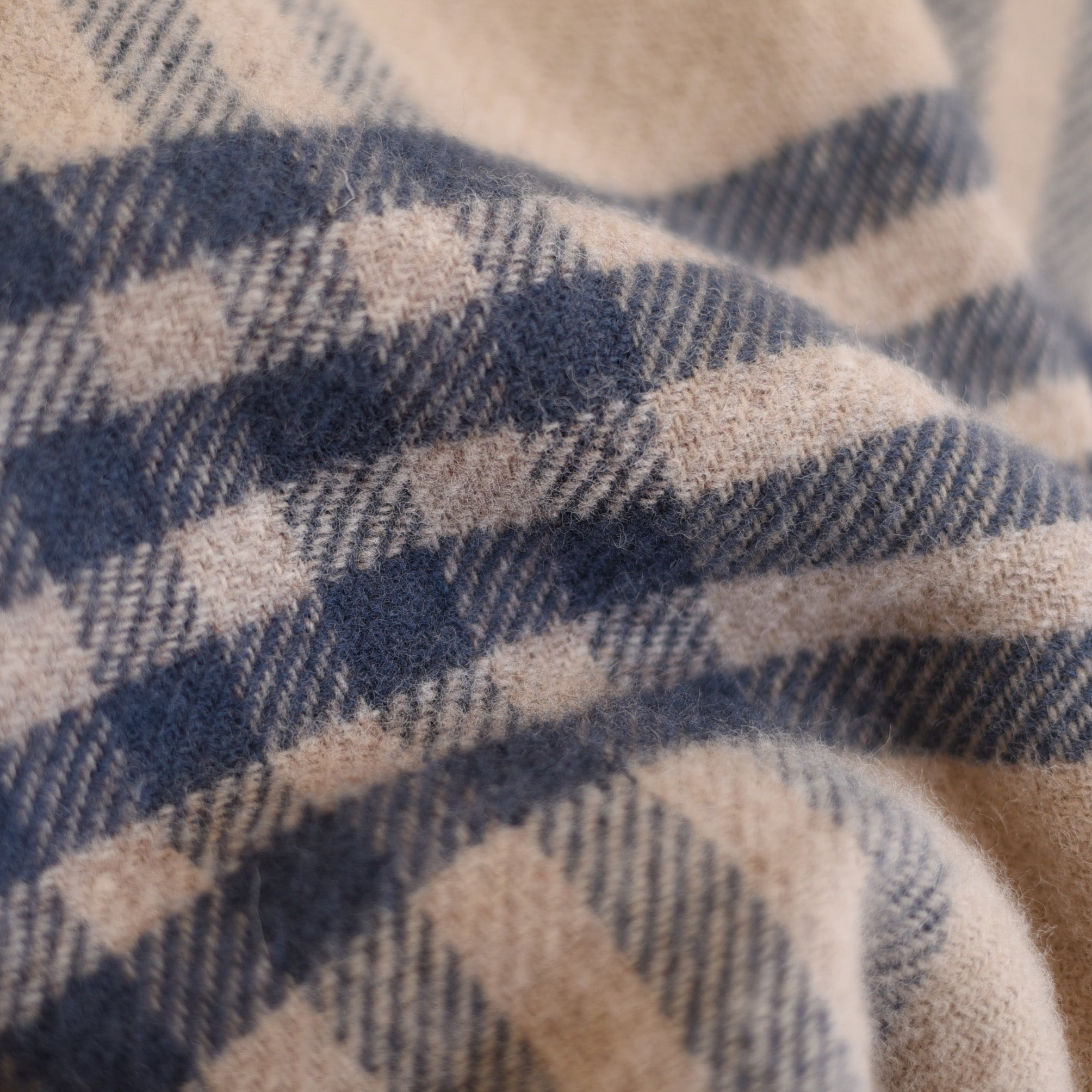 Close-up of the Tarradale Lambswool Throw by Campbells of Beauly, featuring soft beige fabric with blue and gray checks, showcasing the textured folds and exceptional British craftsmanship.