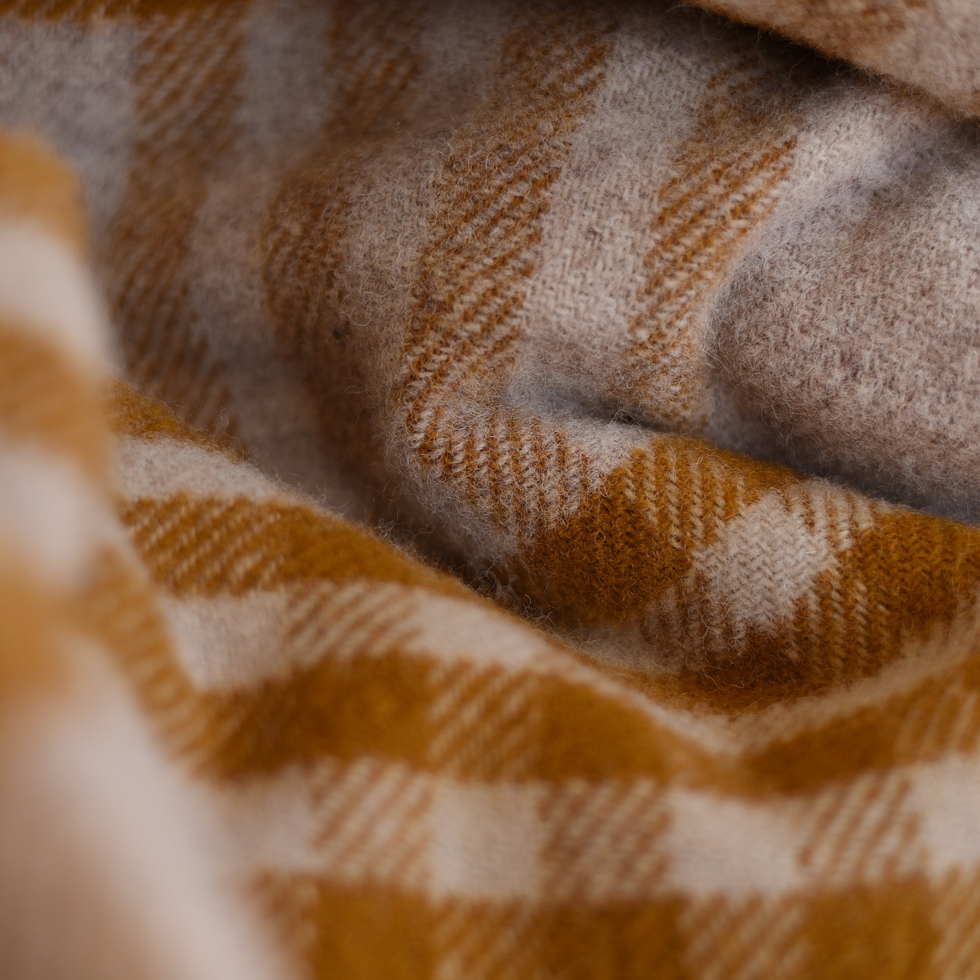 Close-up of the Tarradale Lambswool Throw by Campbells of Beauly, showcasing its soft, fuzzy texture and checked mustard yellow and beige pattern. Expertly crafted in Britain, it appears warm, cozy, and slightly textured with gentle folds.