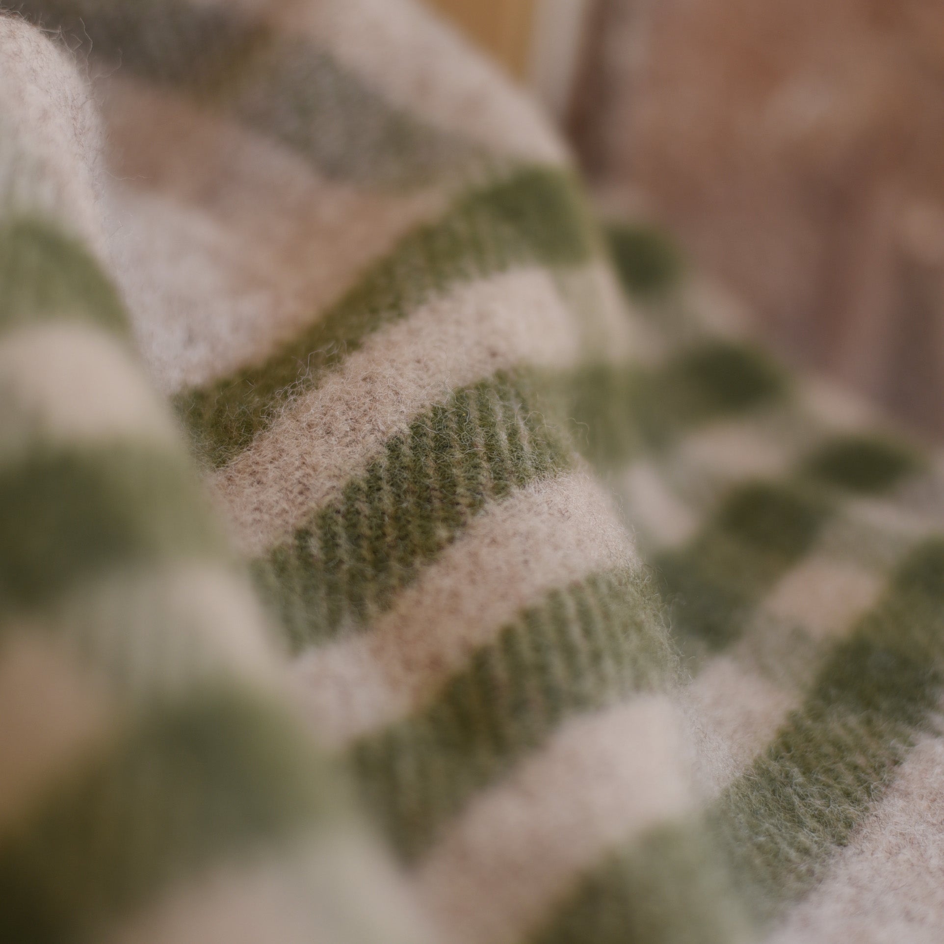 A close-up of the Tarradale Lambswool Throw by Campbells of Beauly, featuring green and beige horizontal stripes that highlight its soft texture, detailed knitting pattern, and fine British craftsmanship.